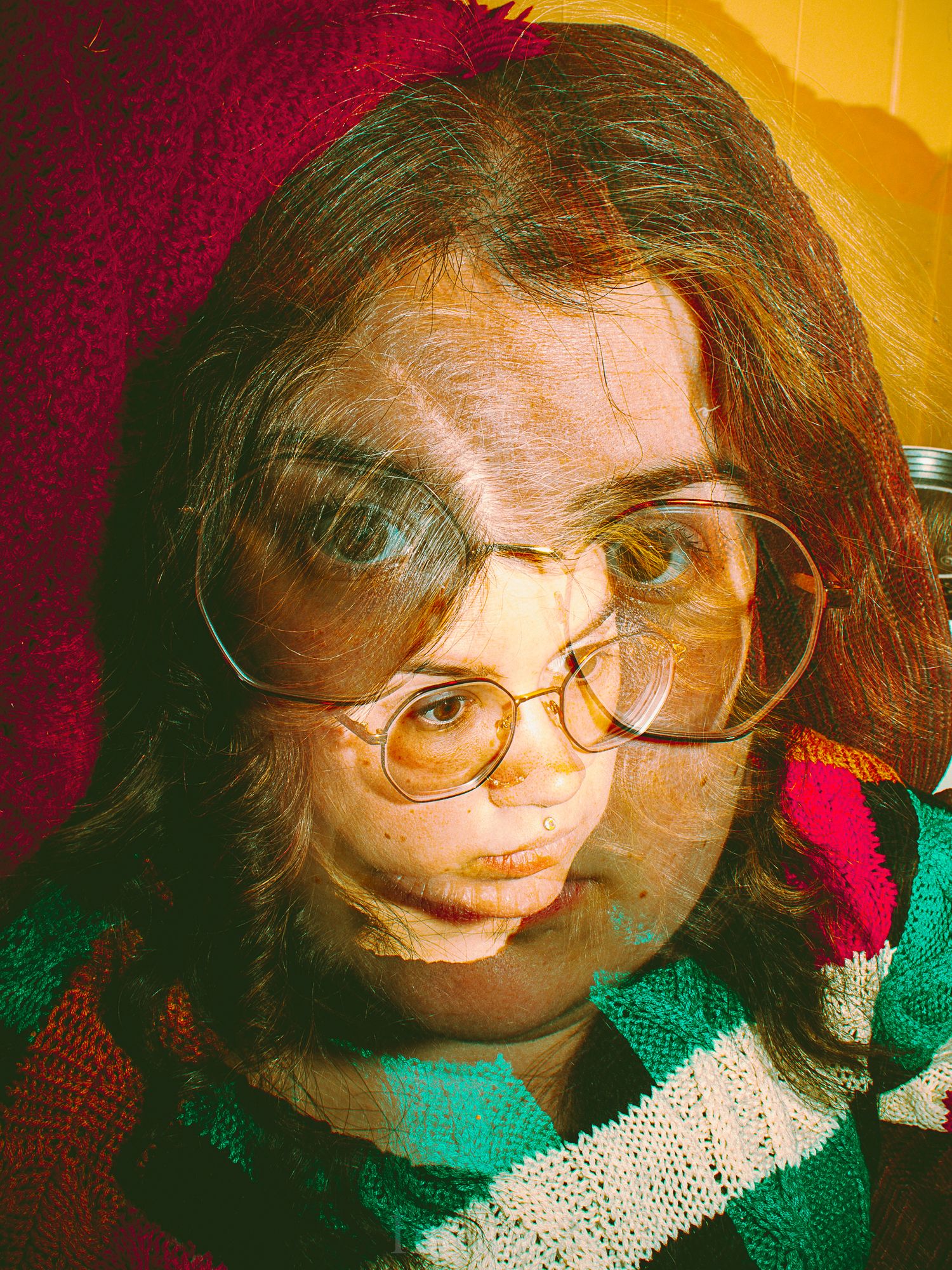 Portrait with warm tones showing glasses and teal sweater against red and yellow background.