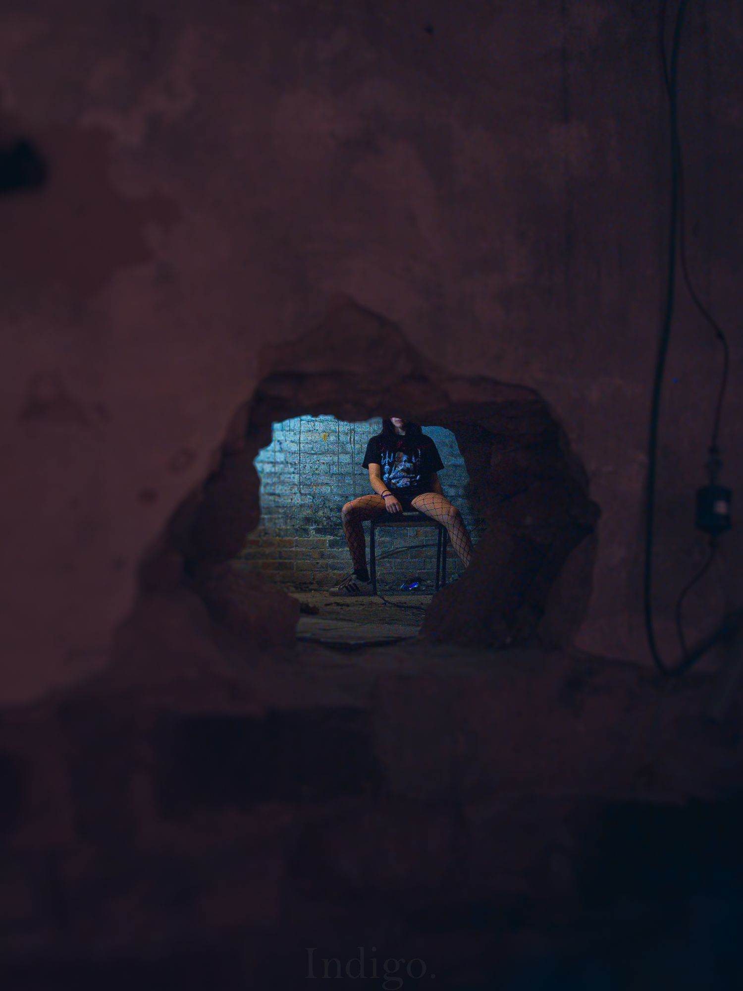 Figure seen through hole in wall with moody blue lighting.