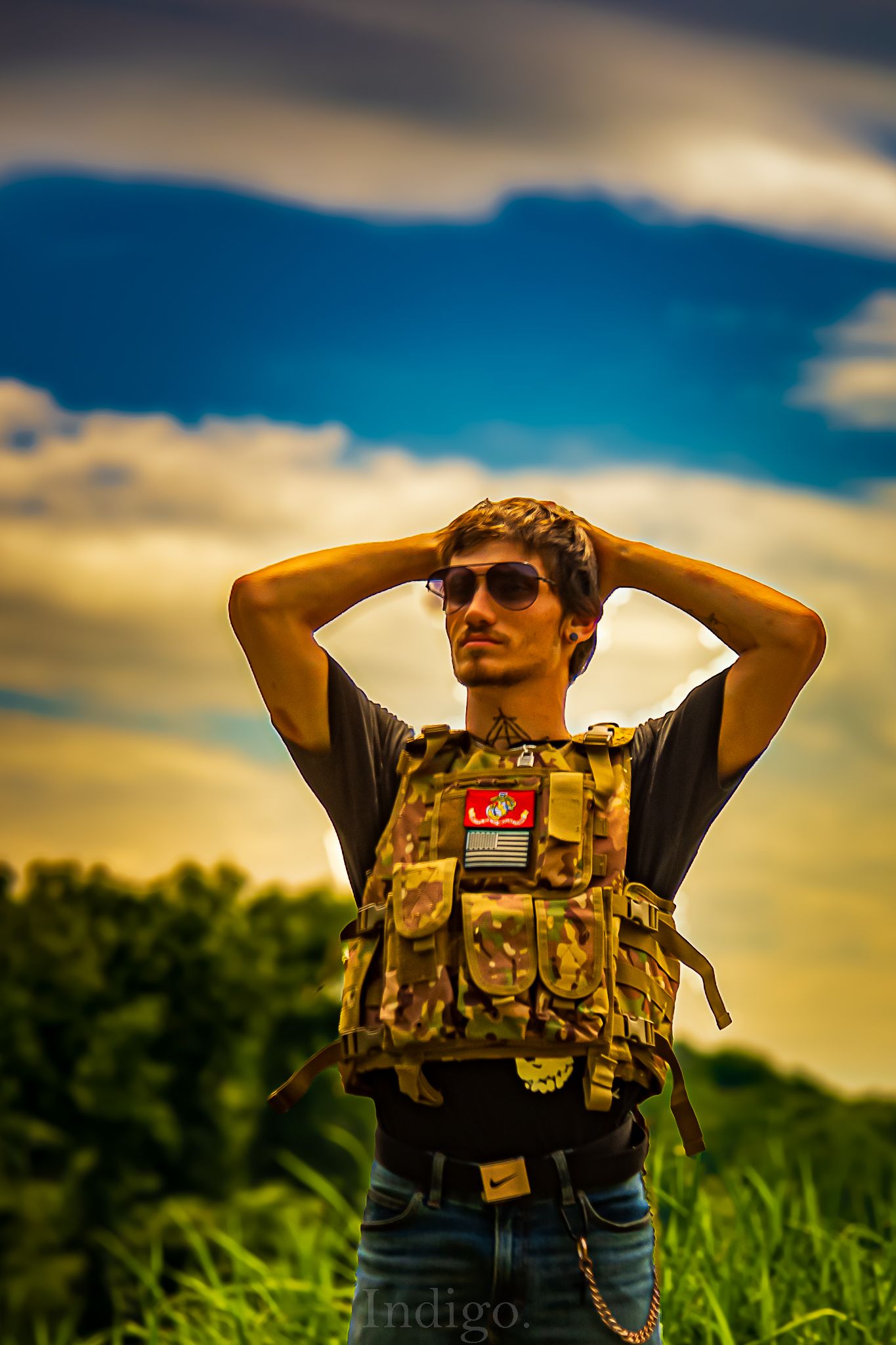 Military tactical gear silhouetted against dramatic sunset and cornfield landscape.