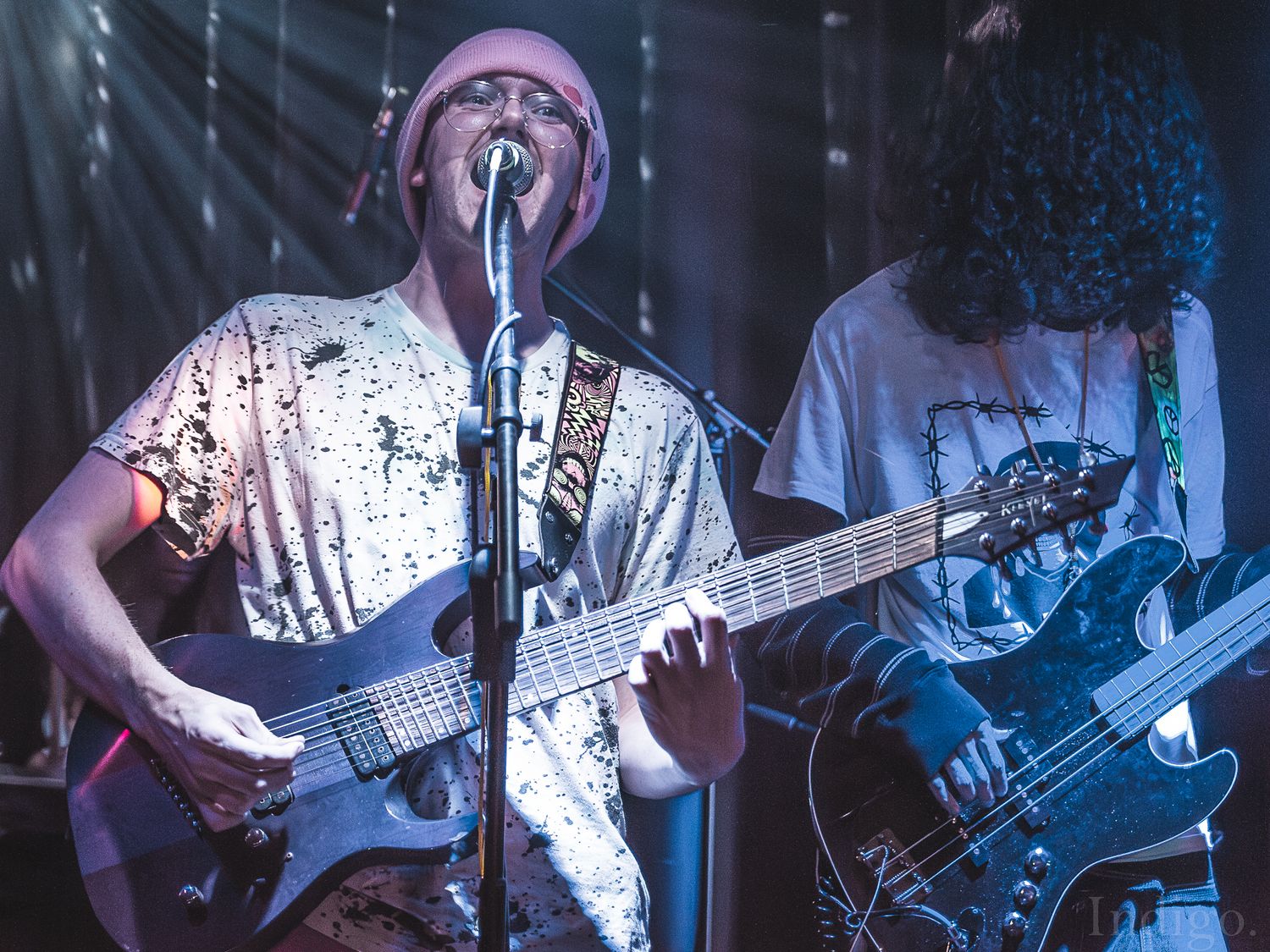 Musicians performing on stage with guitars under blue theatrical lighting.