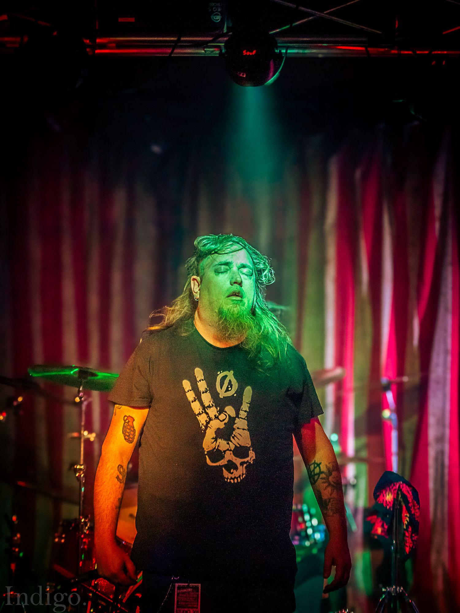 Concert performer illuminated by dramatic green and red stage lighting during an energetic live music performance.