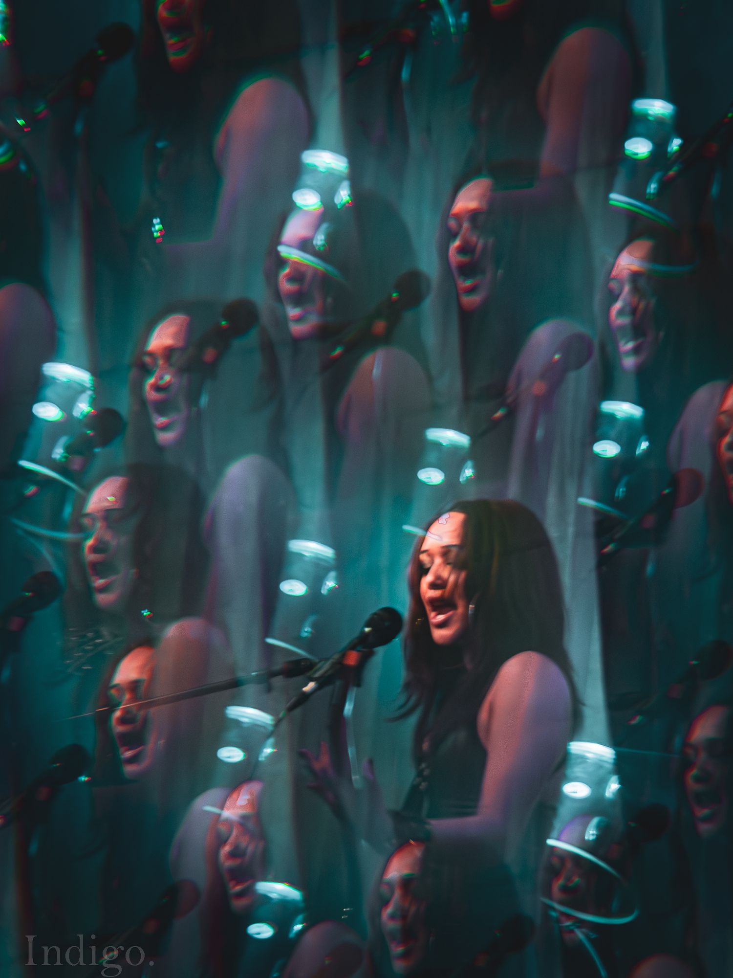 Dramatic concert lighting creates multiple reflections and silhouettes in moody teal and red tones during live performance.