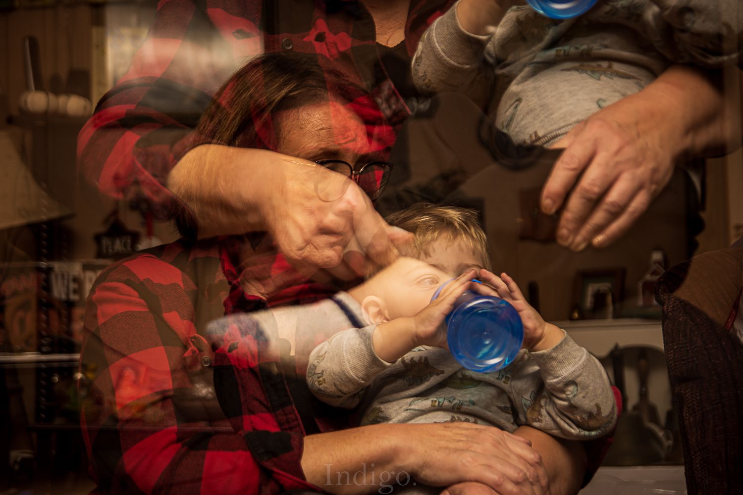 Hands helping a child with a blue cup in a cozy home setting.