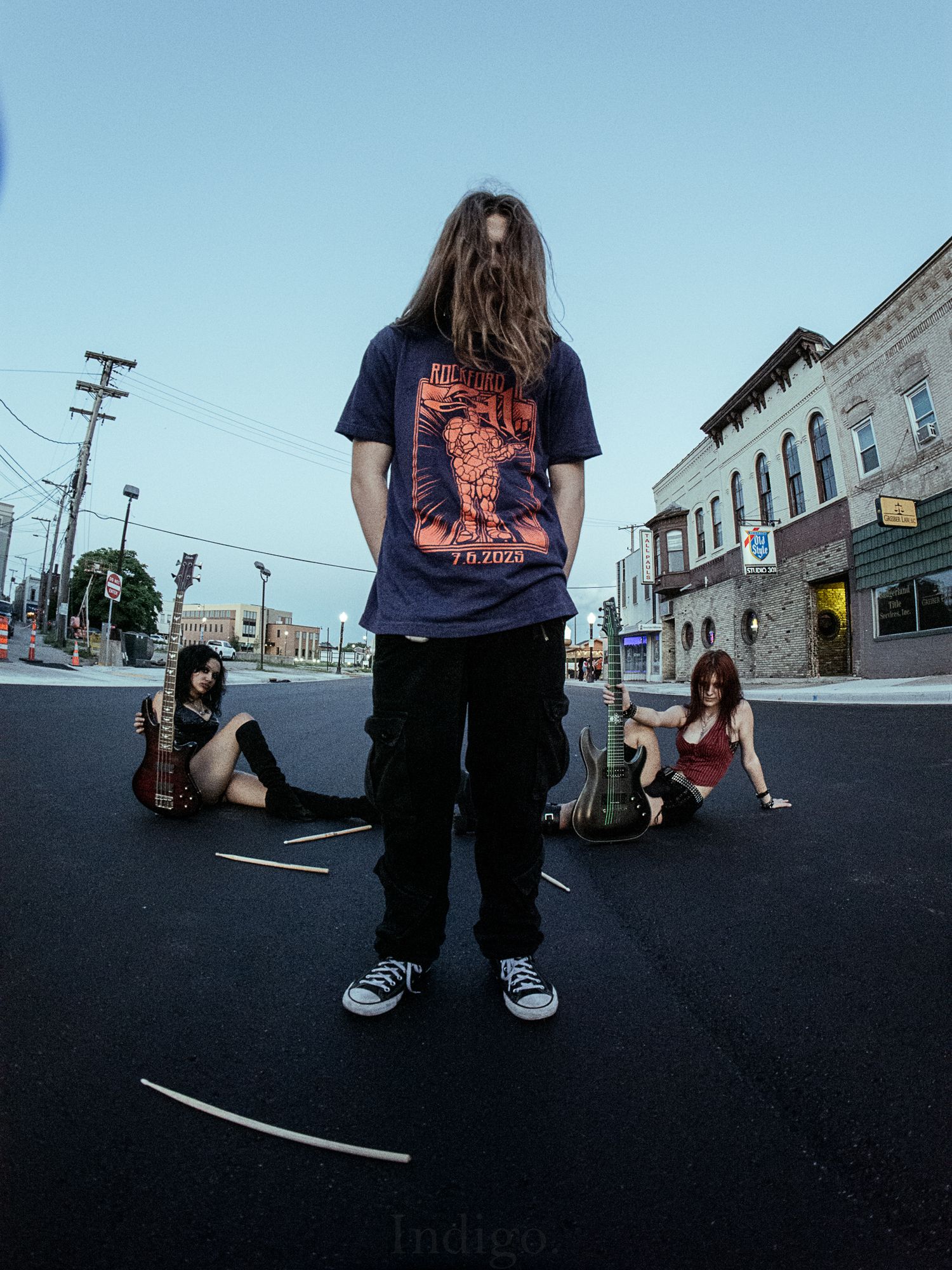 Street scene with musician in blue t-shirt standing on empty road with people sitting.