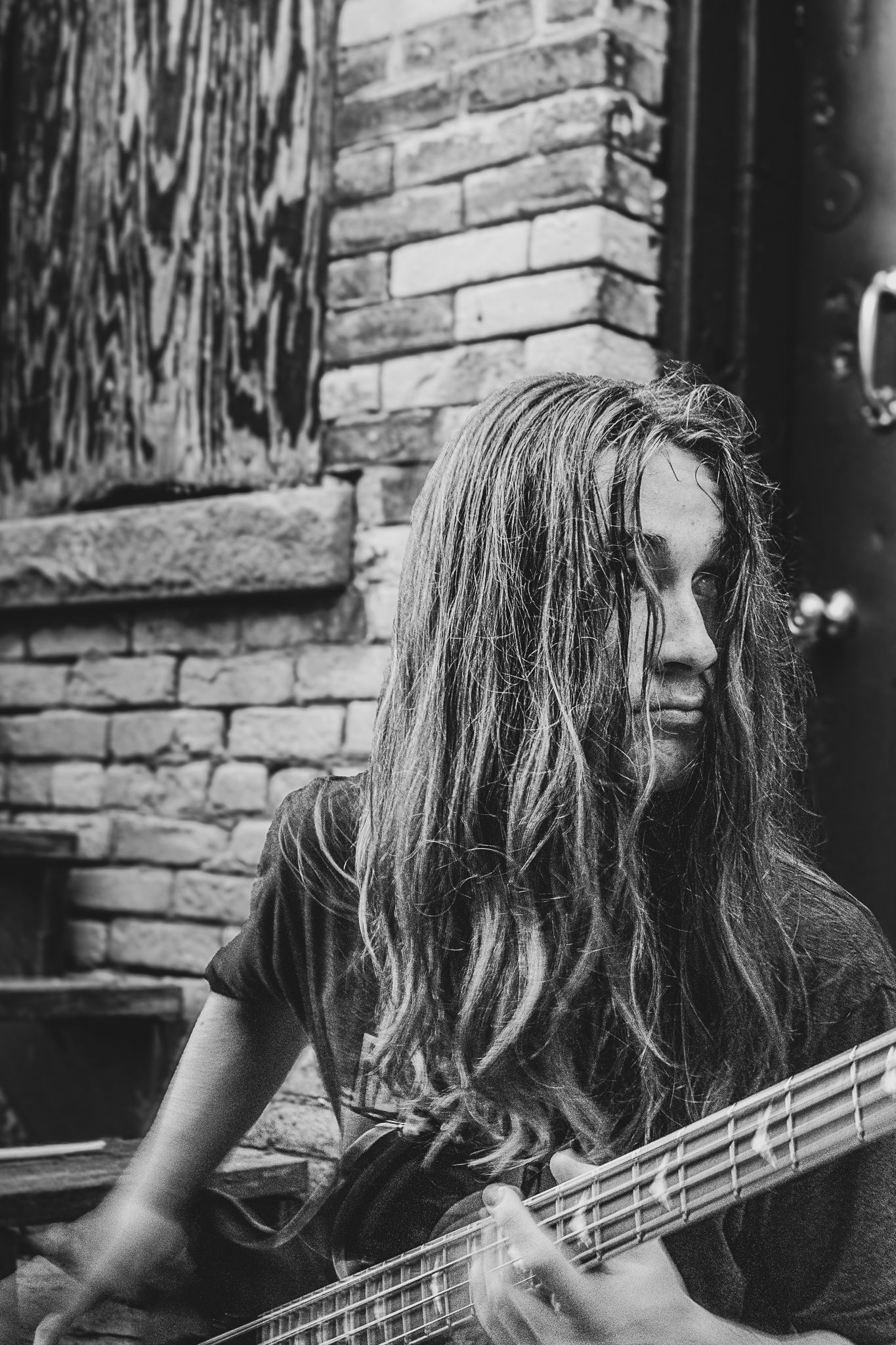 Black and white portrait of bassist playing instrument against brick wall.
