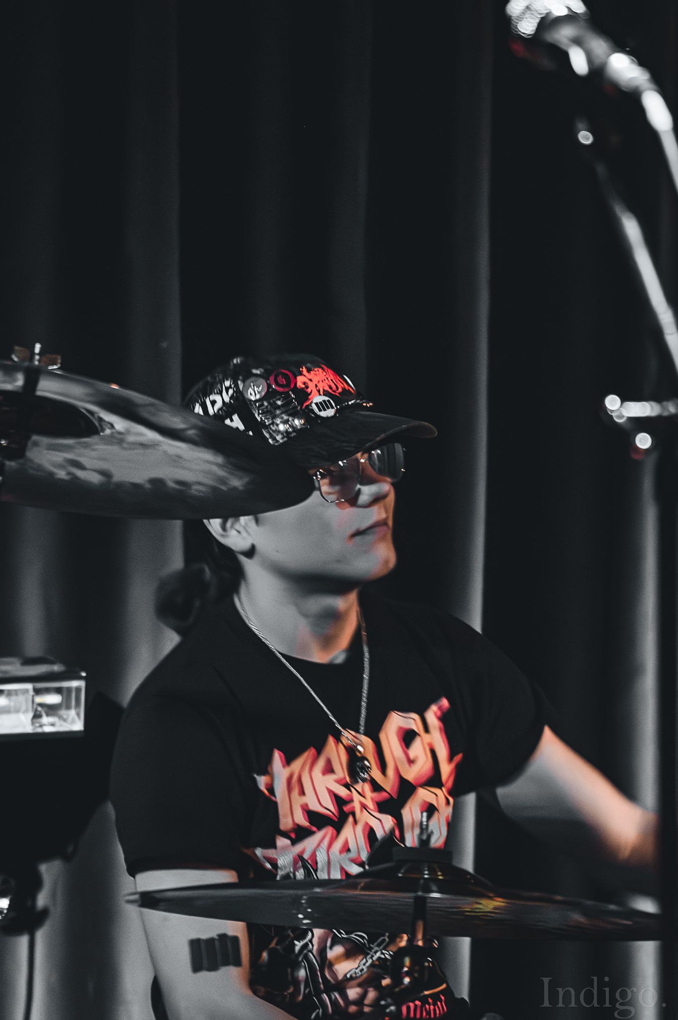 Drummer in black attire performing on stage with dramatic lighting effects.