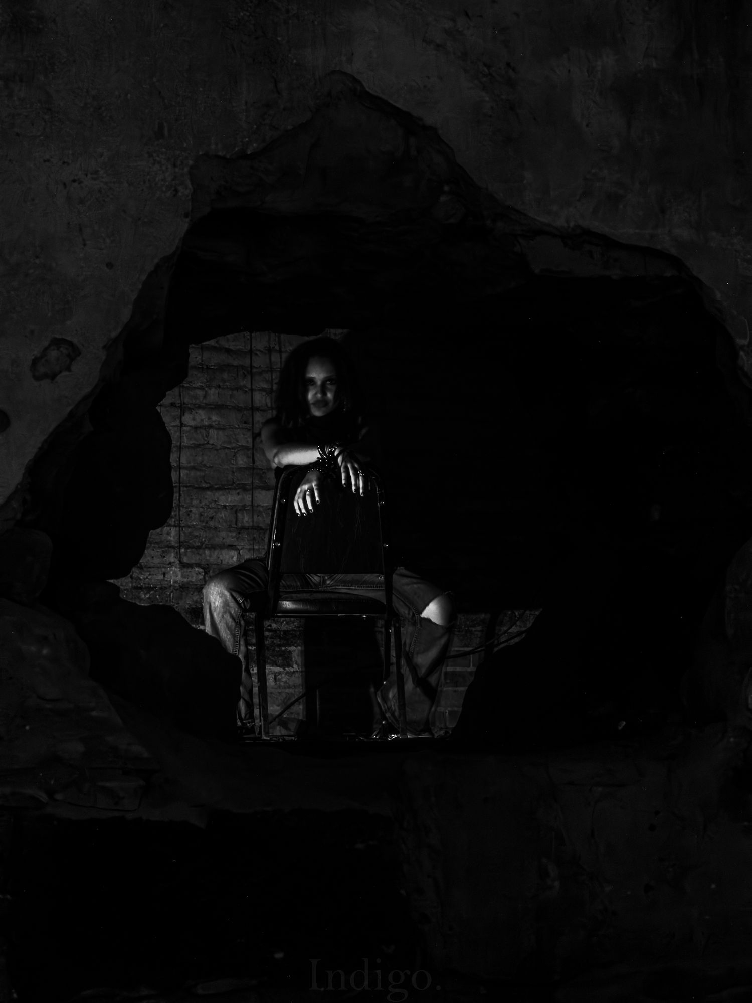 Dramatic black and white photo of figure seated in dark cave-like space.