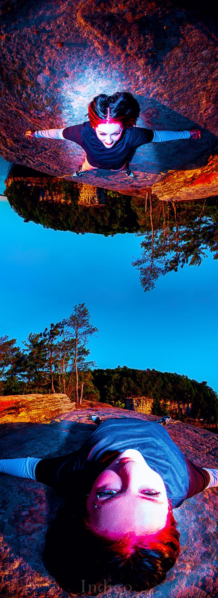 Creative upside-down portrait on a rock formation against bright blue sky with dramatic lighting.