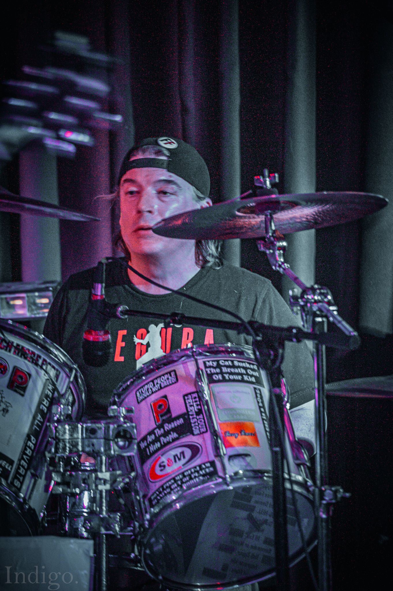 Drummer performing on stage with illuminated drum kit in moody lighting.