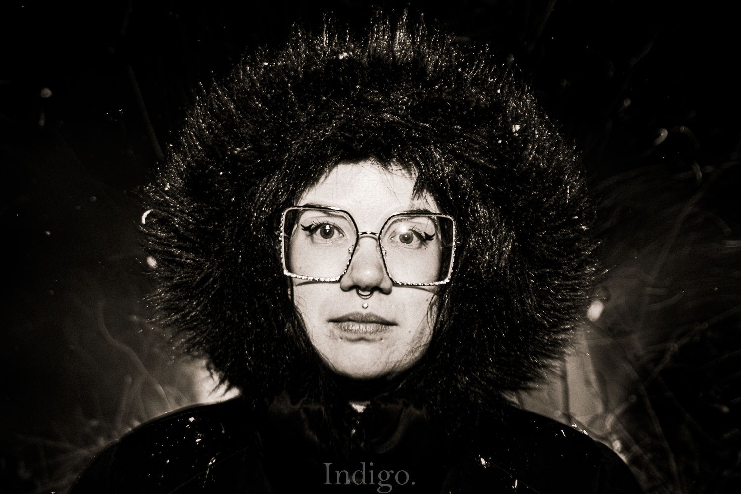Dramatic black and white portrait with glasses against dark background.