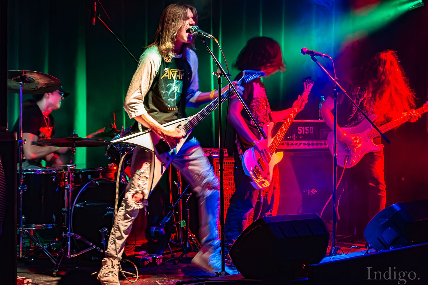 Rock band performing on stage with dramatic colorful lighting and silhouetted musicians.