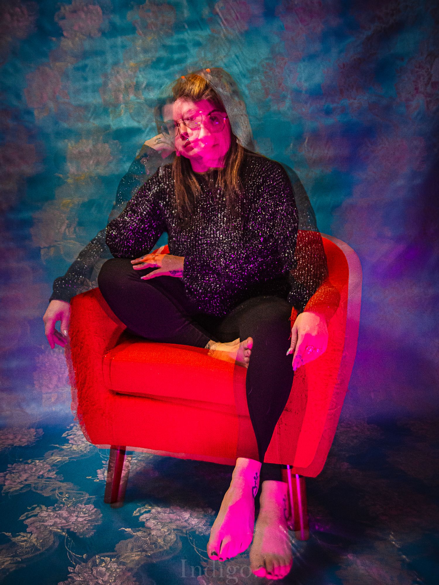 Vibrant photoshoot featuring a red couch against colorful neon pink and blue lighting effects.