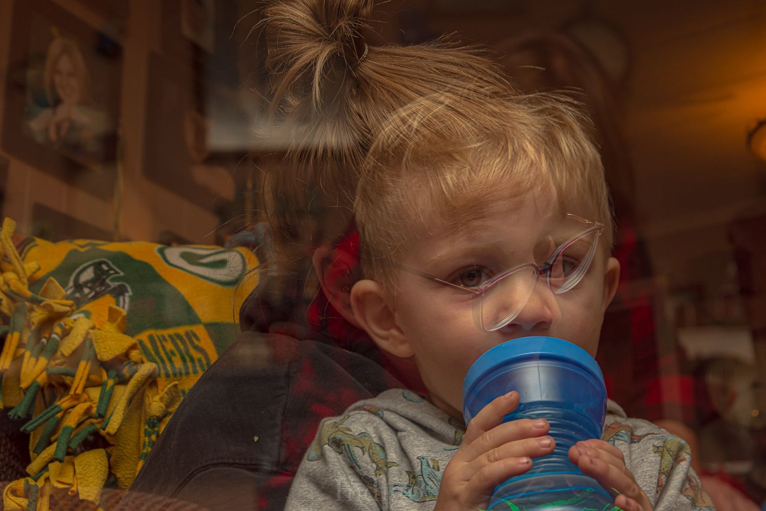 Child drinking from a blue sippy cup in warm indoor lighting.
