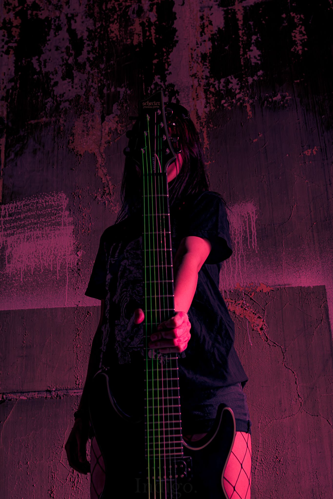 Dark silhouette of a guitar neck illuminated by moody purple and red lighting.