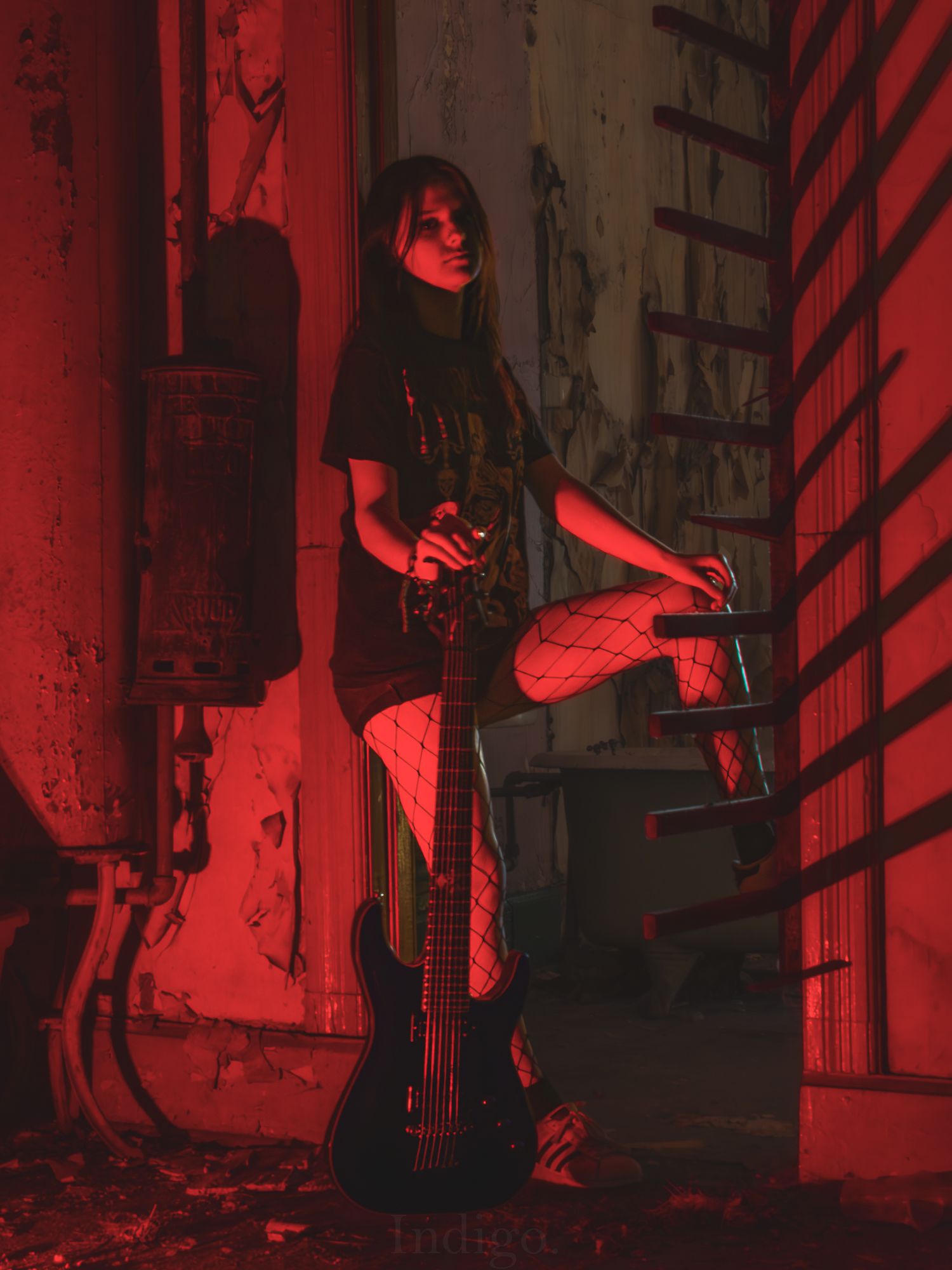 Musician with bass guitar posing in industrial setting with red lighting.