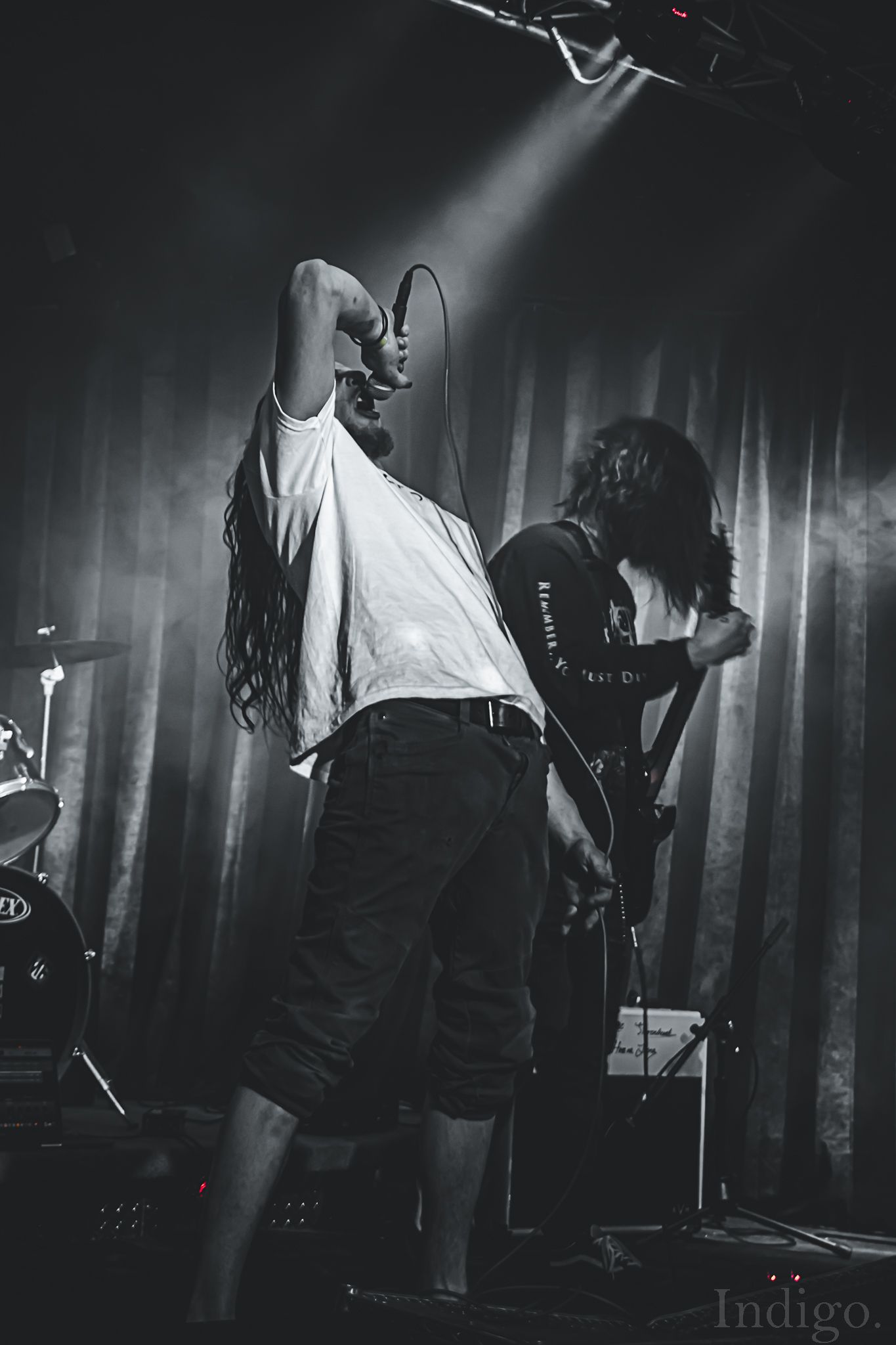 Atmospheric black and white concert photo showing performers in silhouette with dramatic stage lighting.