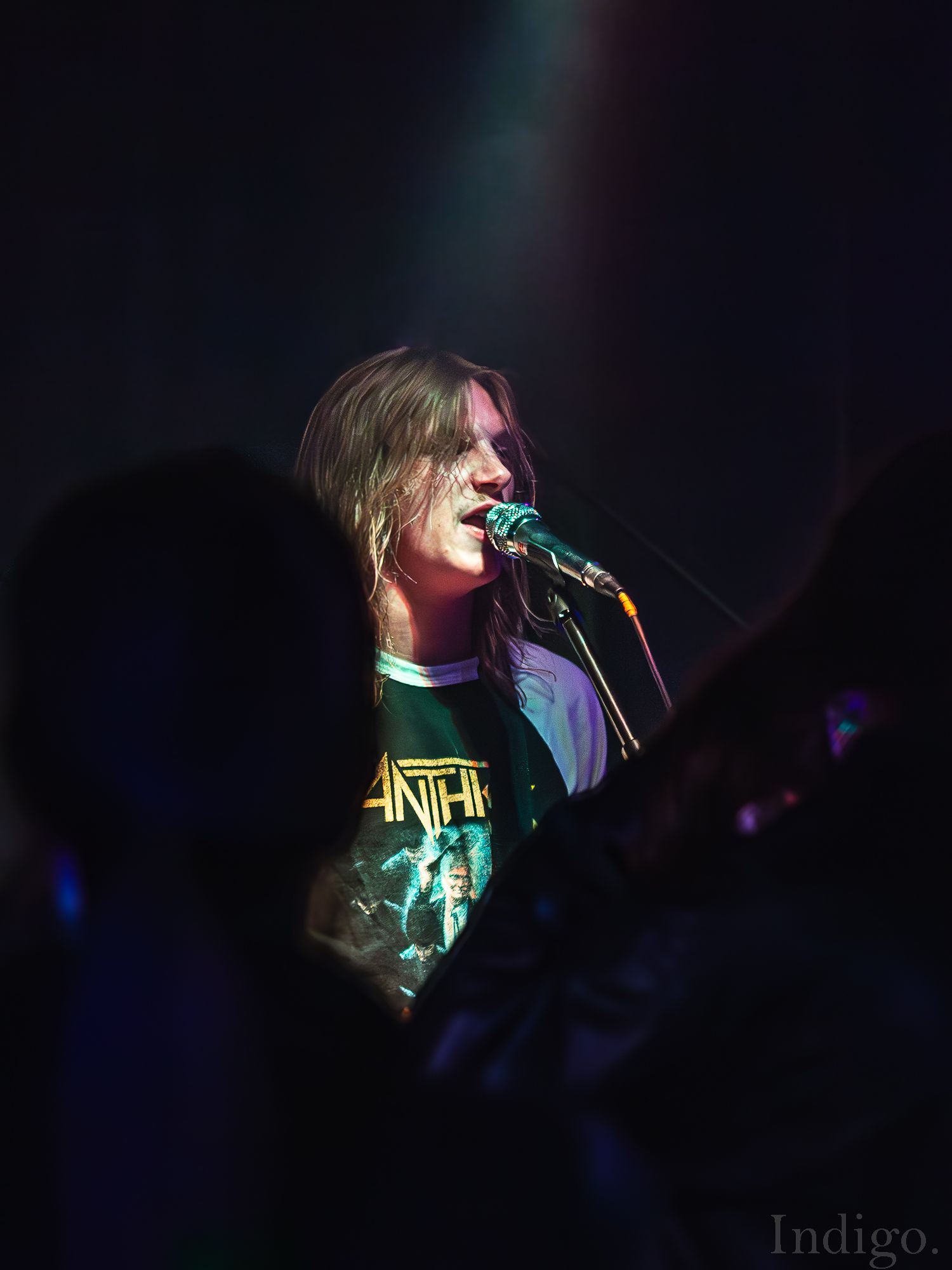 Silhouetted performer singing on dimly lit stage with colored lighting effects.