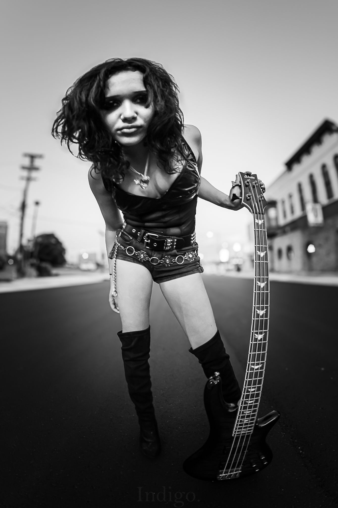 Rock musician posing with bass guitar on empty street in black and white.
