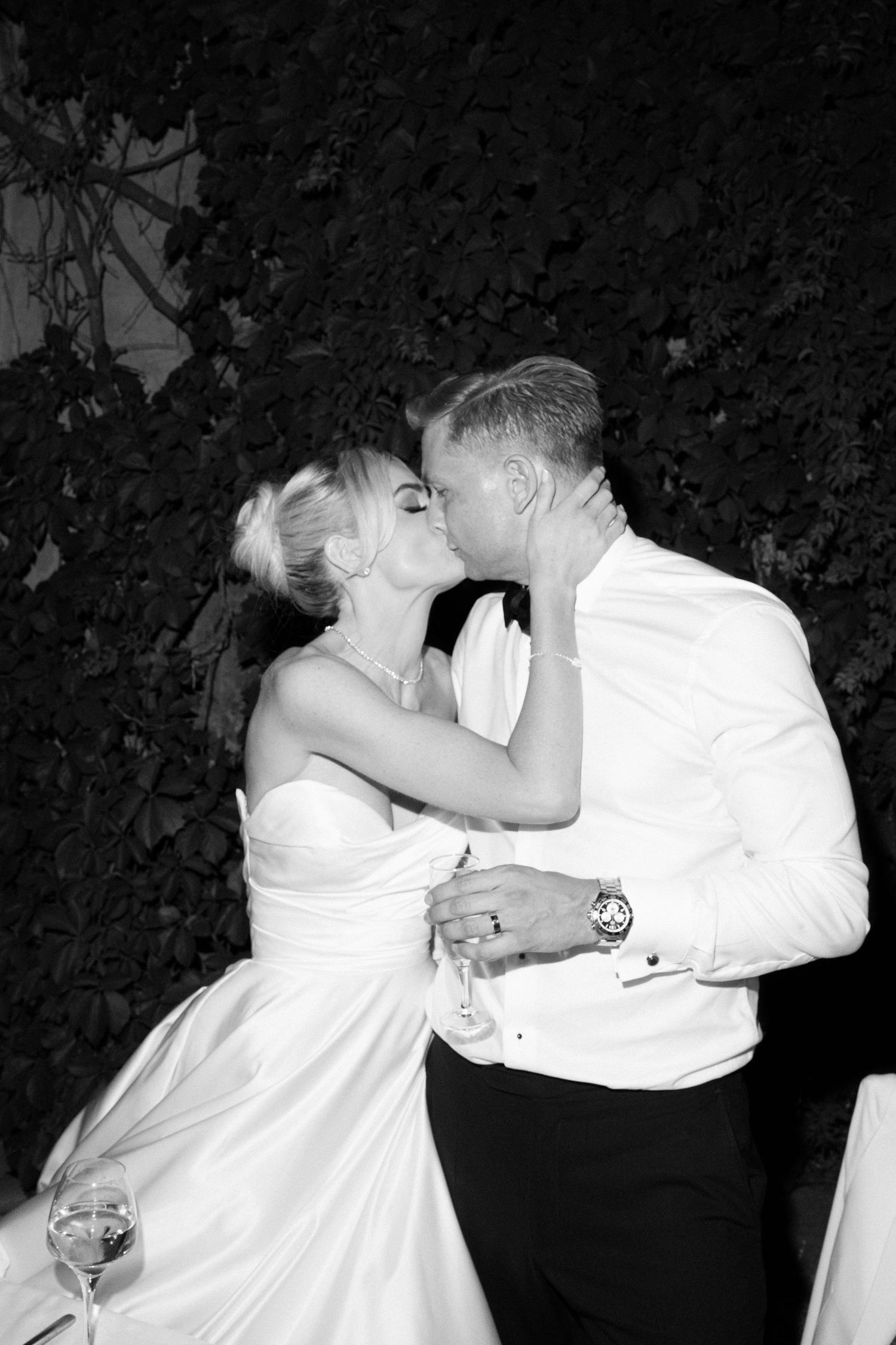 Black and white photo of a bride and groom sharing a romantic kiss at their wedding reception outdoors.
