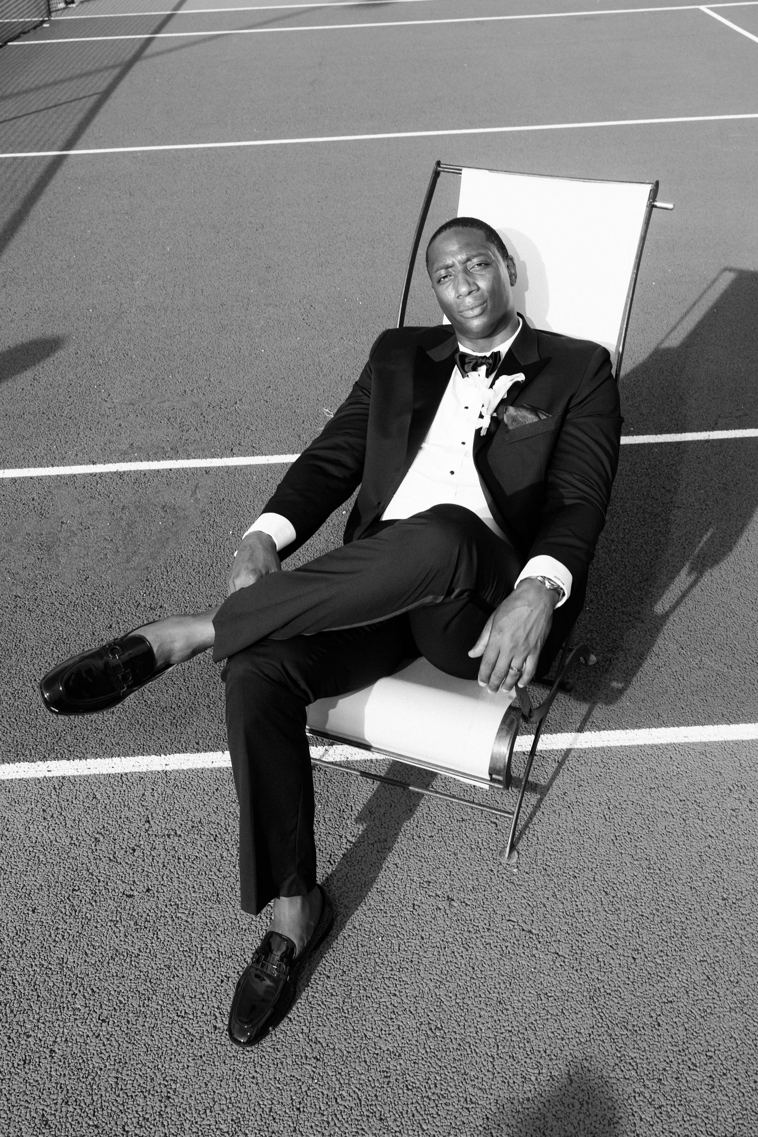 Elegant man in tuxedo relaxing on chair on tennis court, black and white fashion photography.