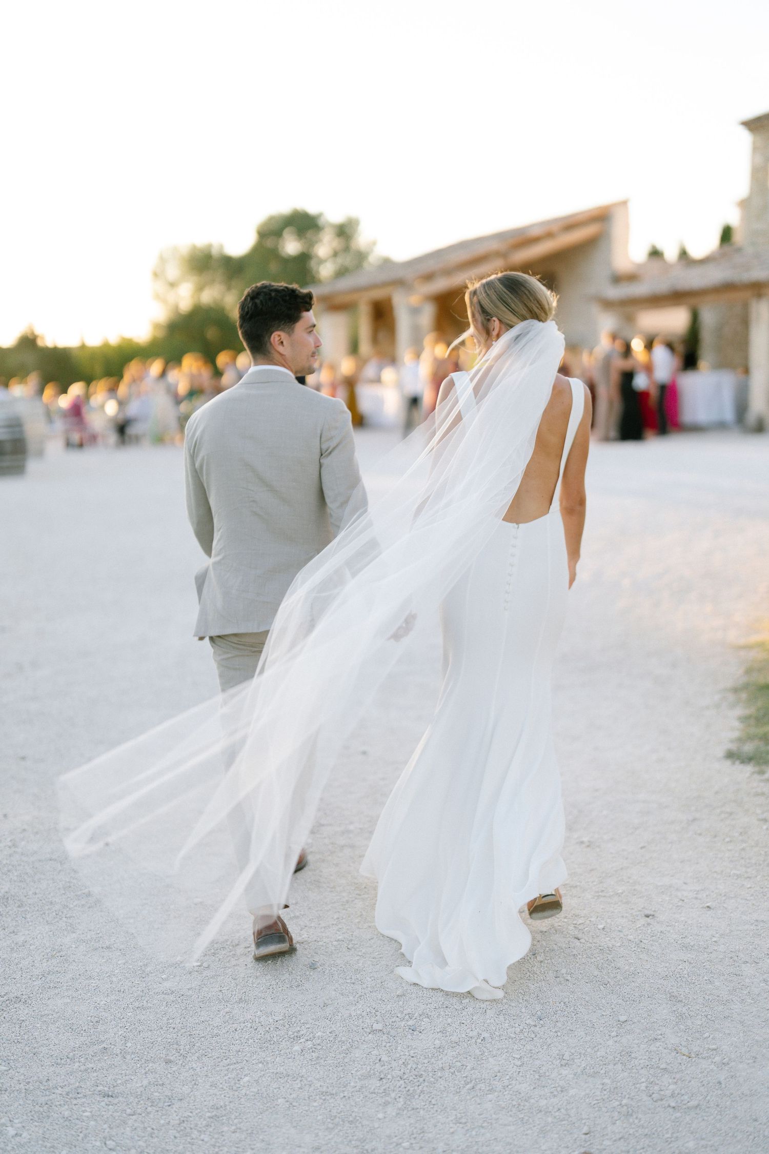 Wedding couple walking on sandy path with flowing white dress in evening light.