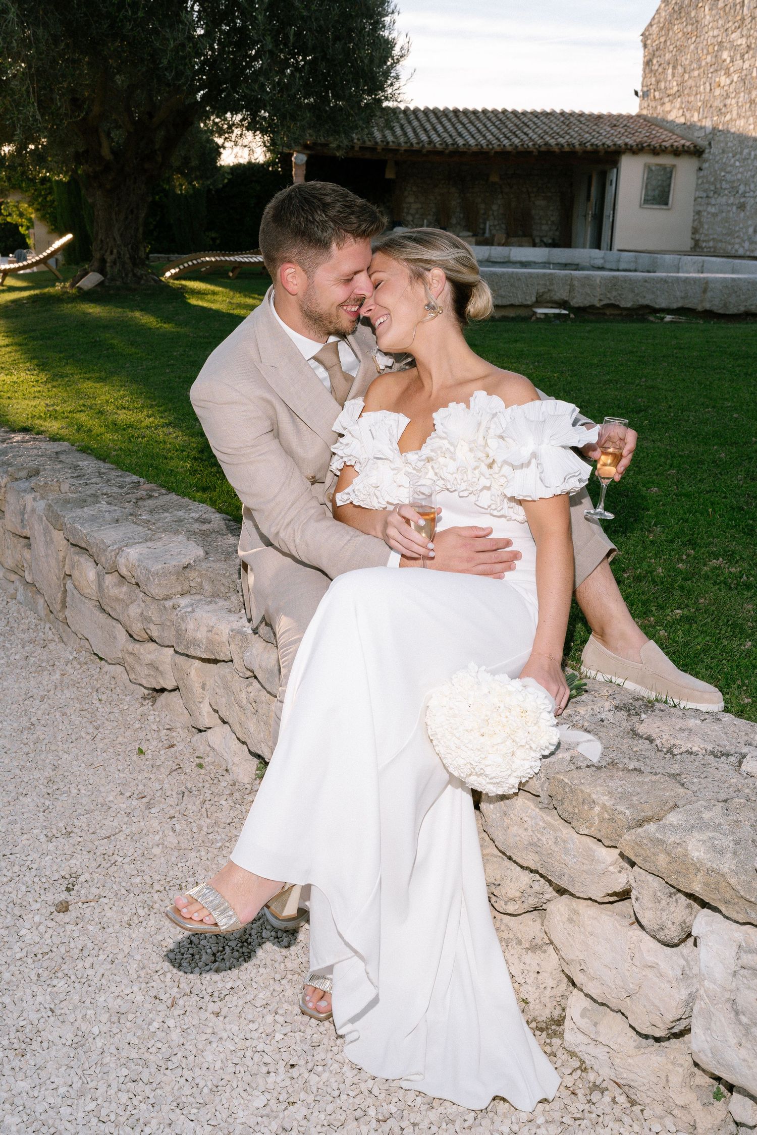 Romantic wedding couple sharing intimate moments on rustic stone wall at sunset.