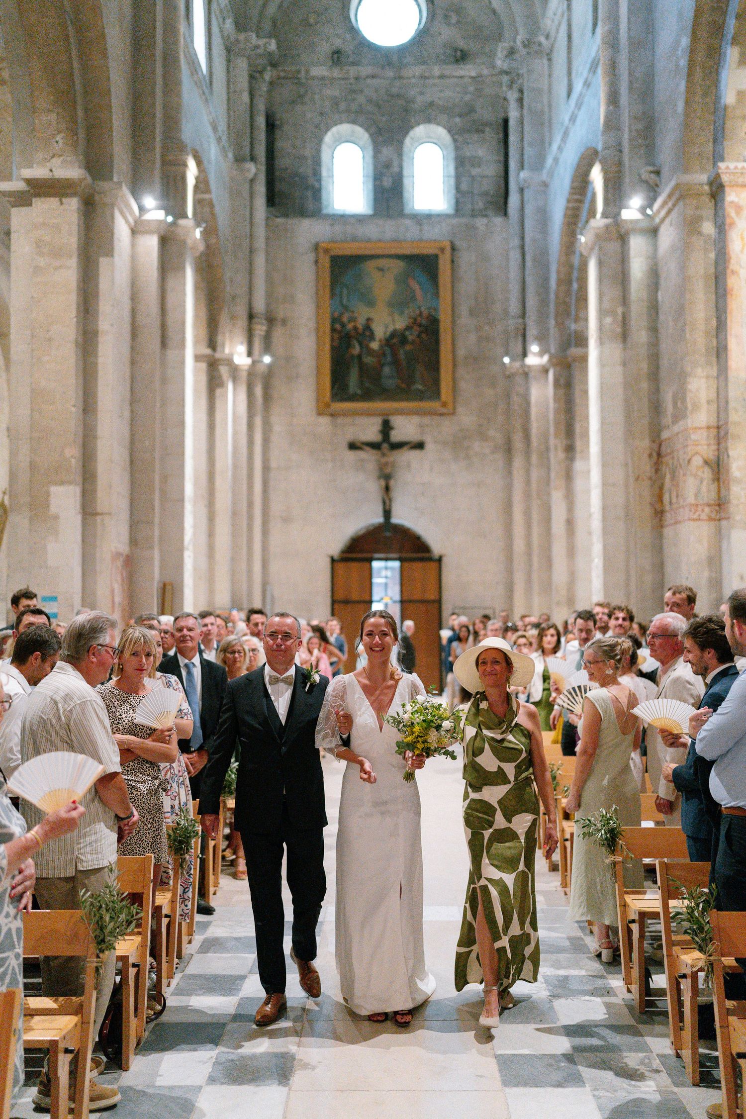 Wedding guests gather inside a bright, ornate church with stone columns and high ceilings.