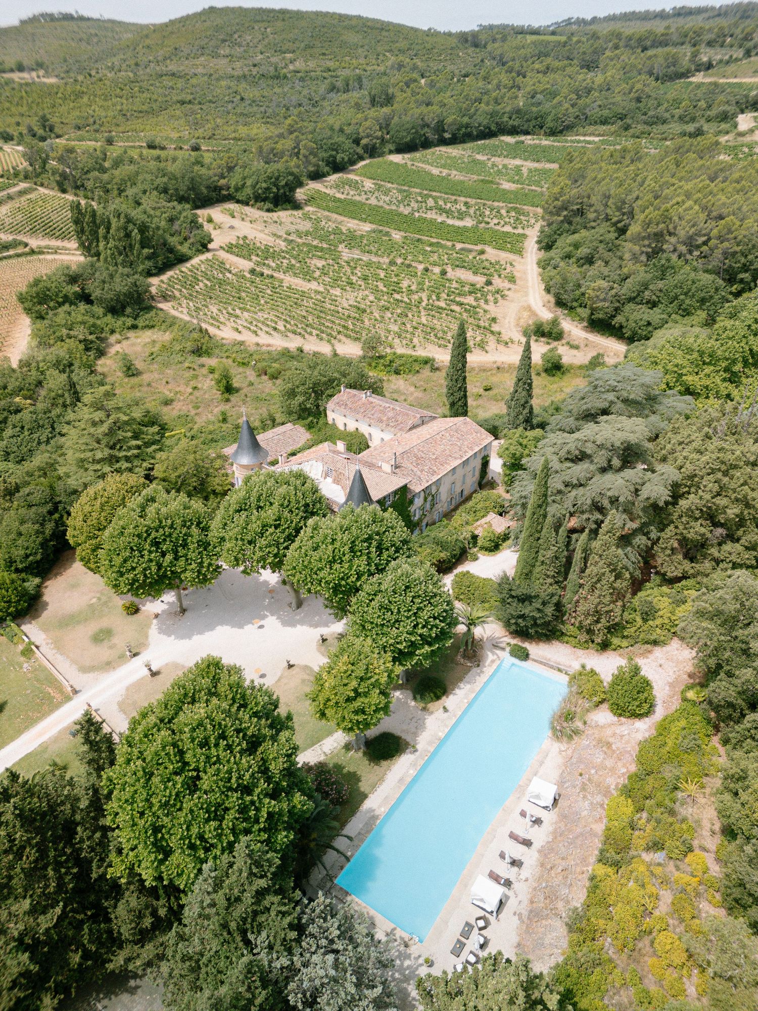 Aerial drone view of a luxury villa property with swimming pool nestled in green hills and vineyards.