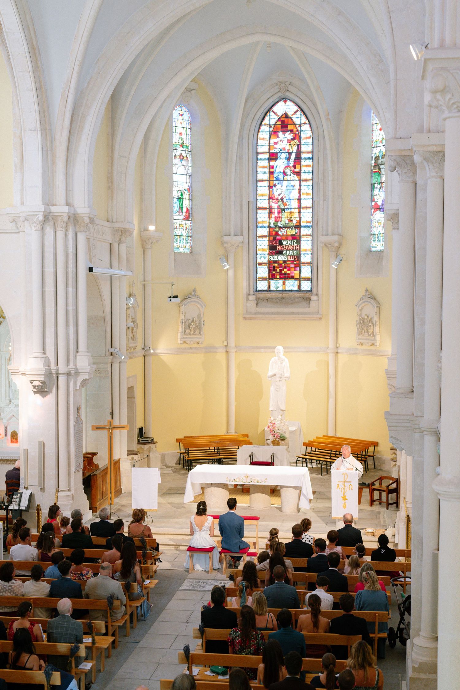 Interior of a Gothic church with stained glass windows and arched ceilings during a ceremony.