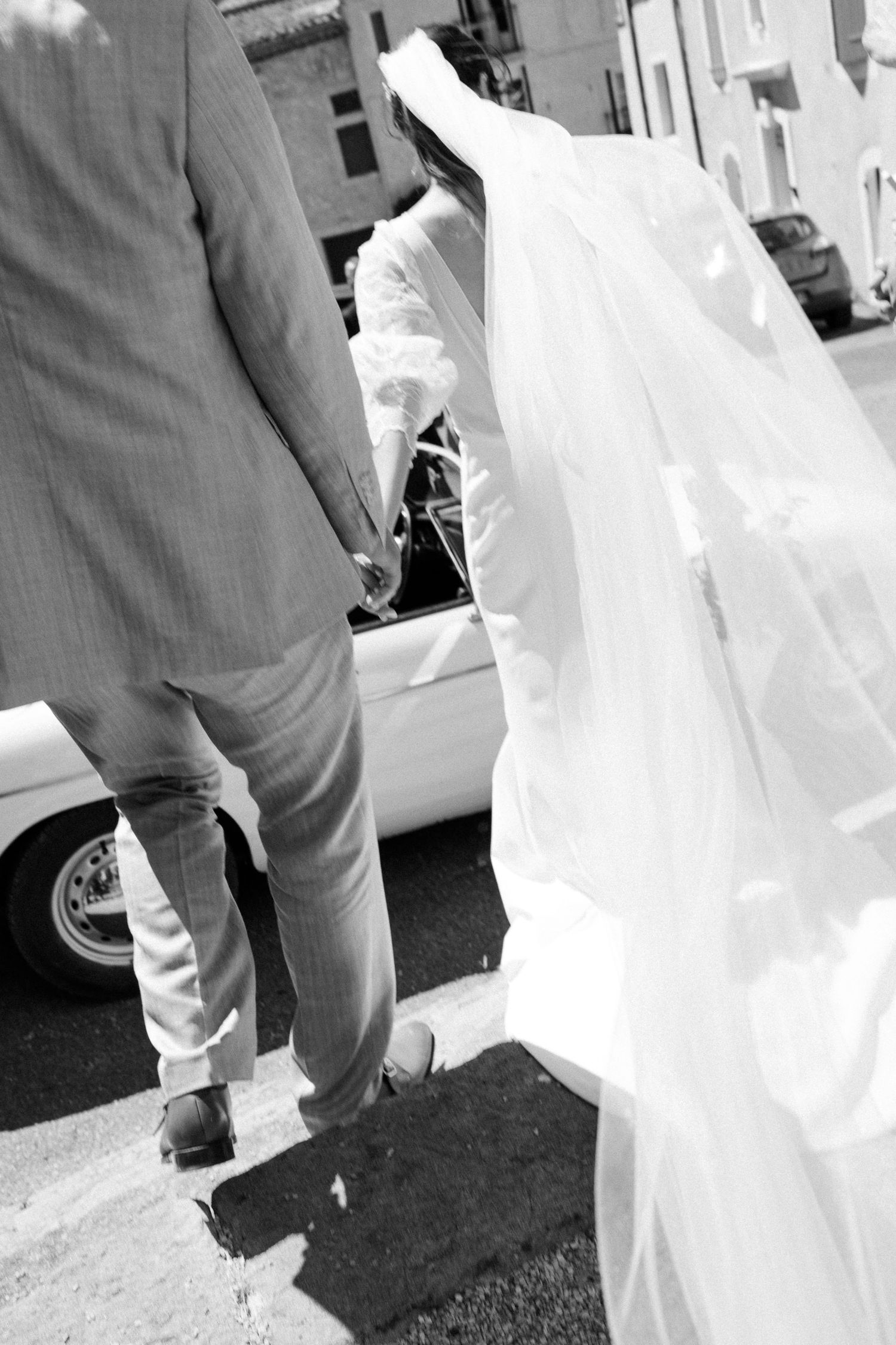 Black and white detail shot of wedding dress train trailing on dark ground.