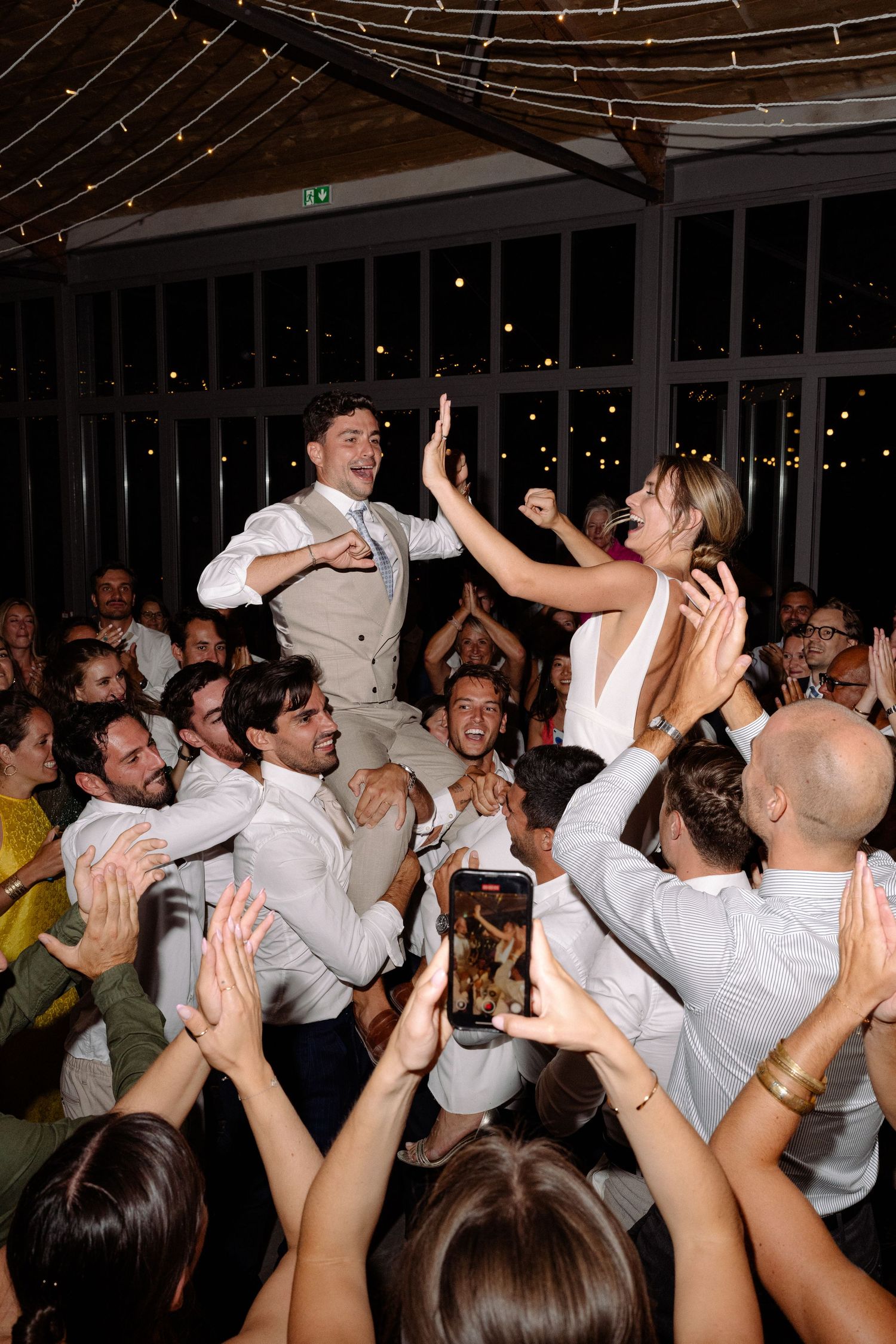 Energetic wedding reception crowd lifts someone up during a dance party.