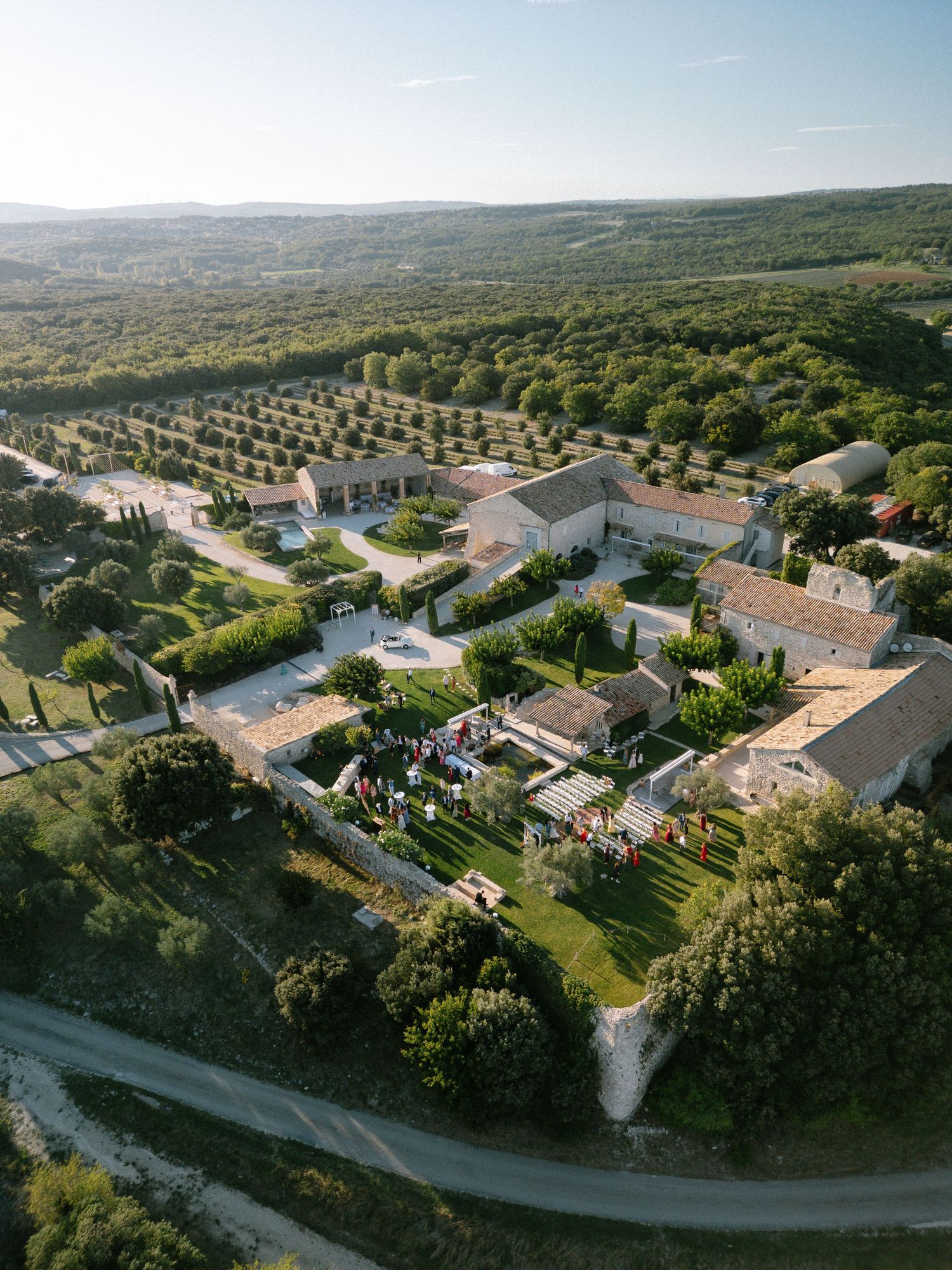 Aerial panoramic view of a Mediterranean resort complex with white buildings and lush gardens nestled in rolling hills.