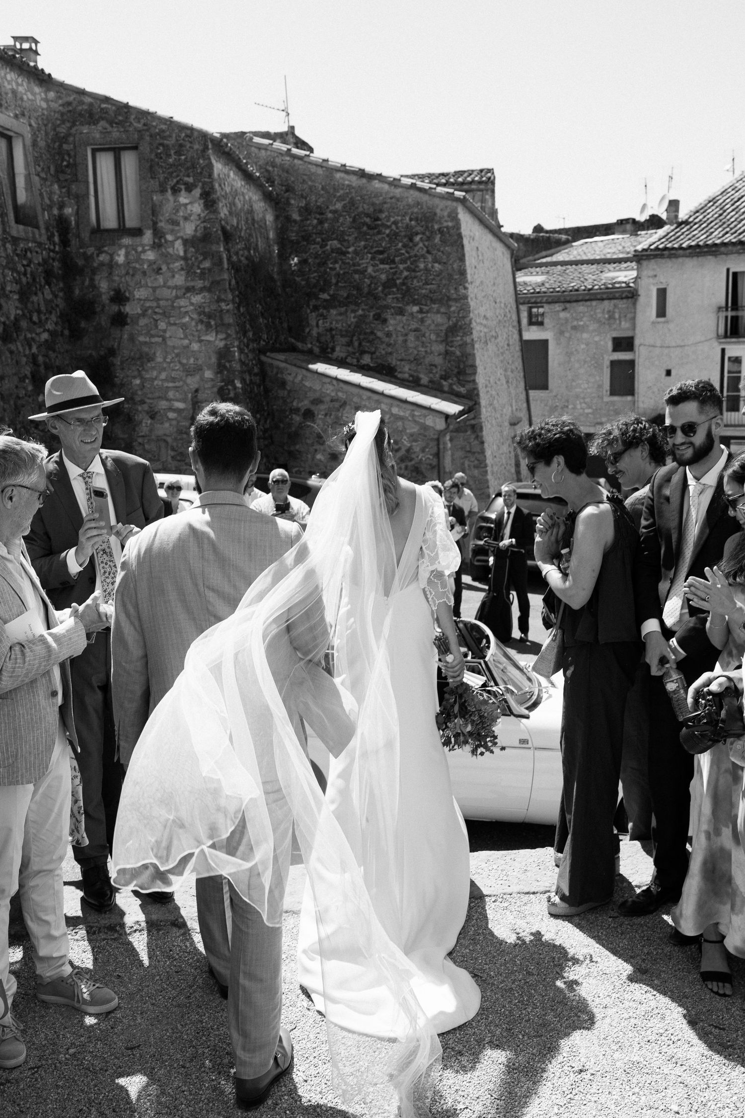 Wedding celebration outdoors with guests in white attire gathering in a stone courtyard.
