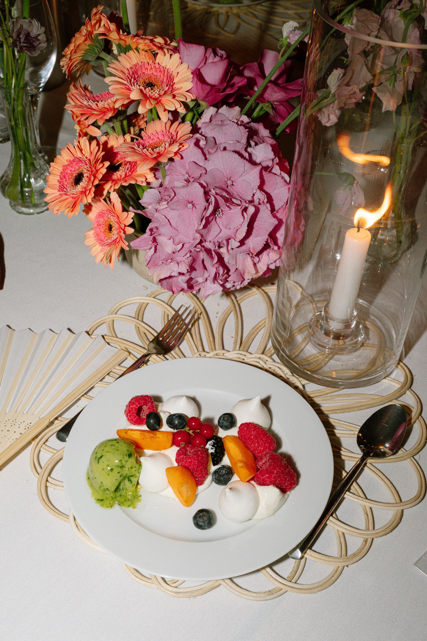 Elegant place setting with coral flowers and fresh fruit on decorative gold-rimmed plate.
