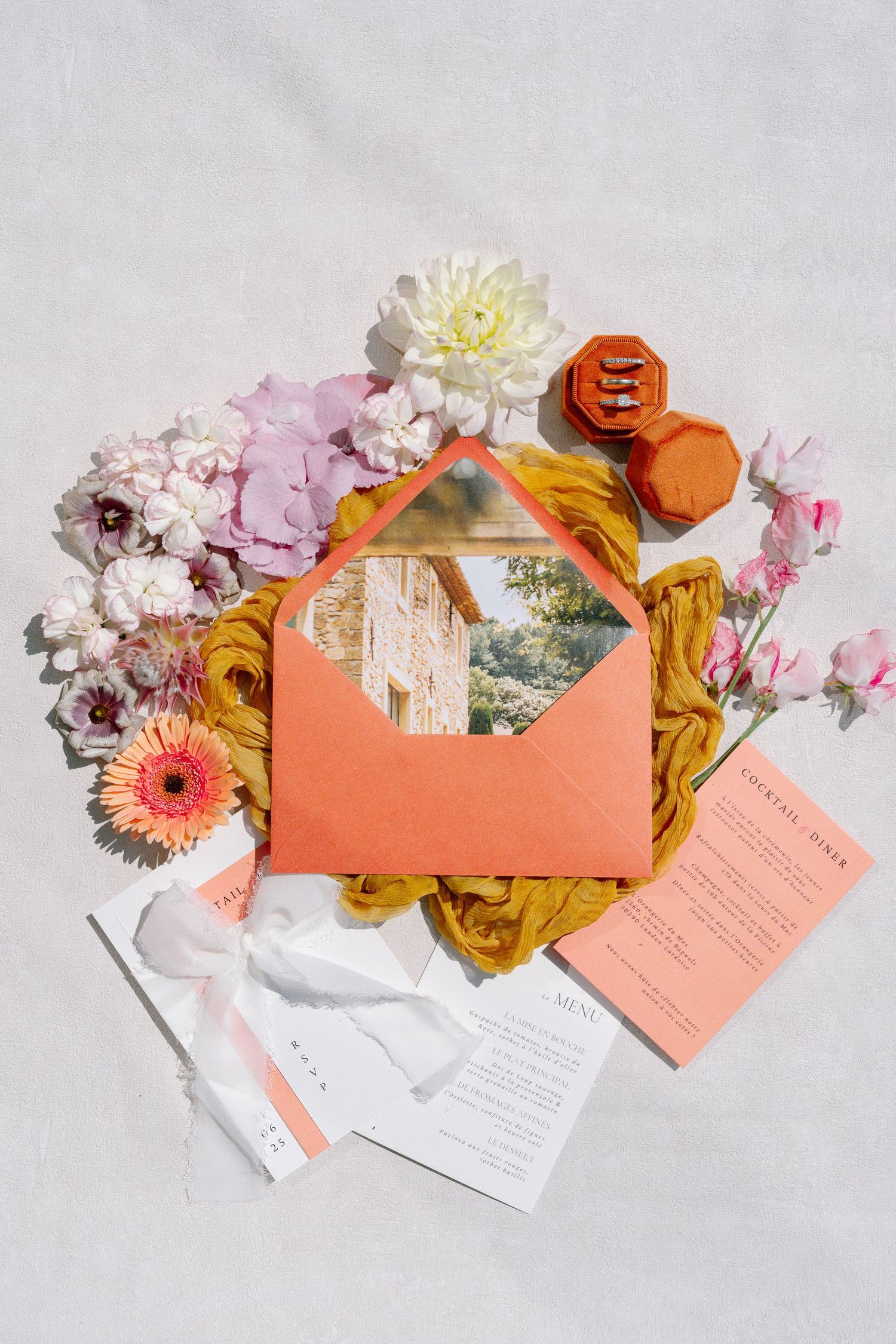 Wedding invitation suite in coral with fresh flowers and golden accents on white background.
