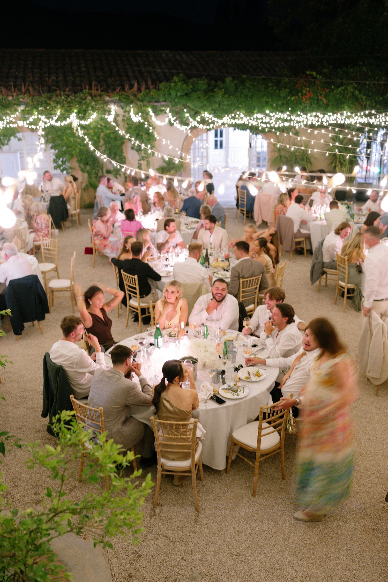 Elegant outdoor wedding reception at night with string lights, round tables, and guests dining under a vine-covered pergola.