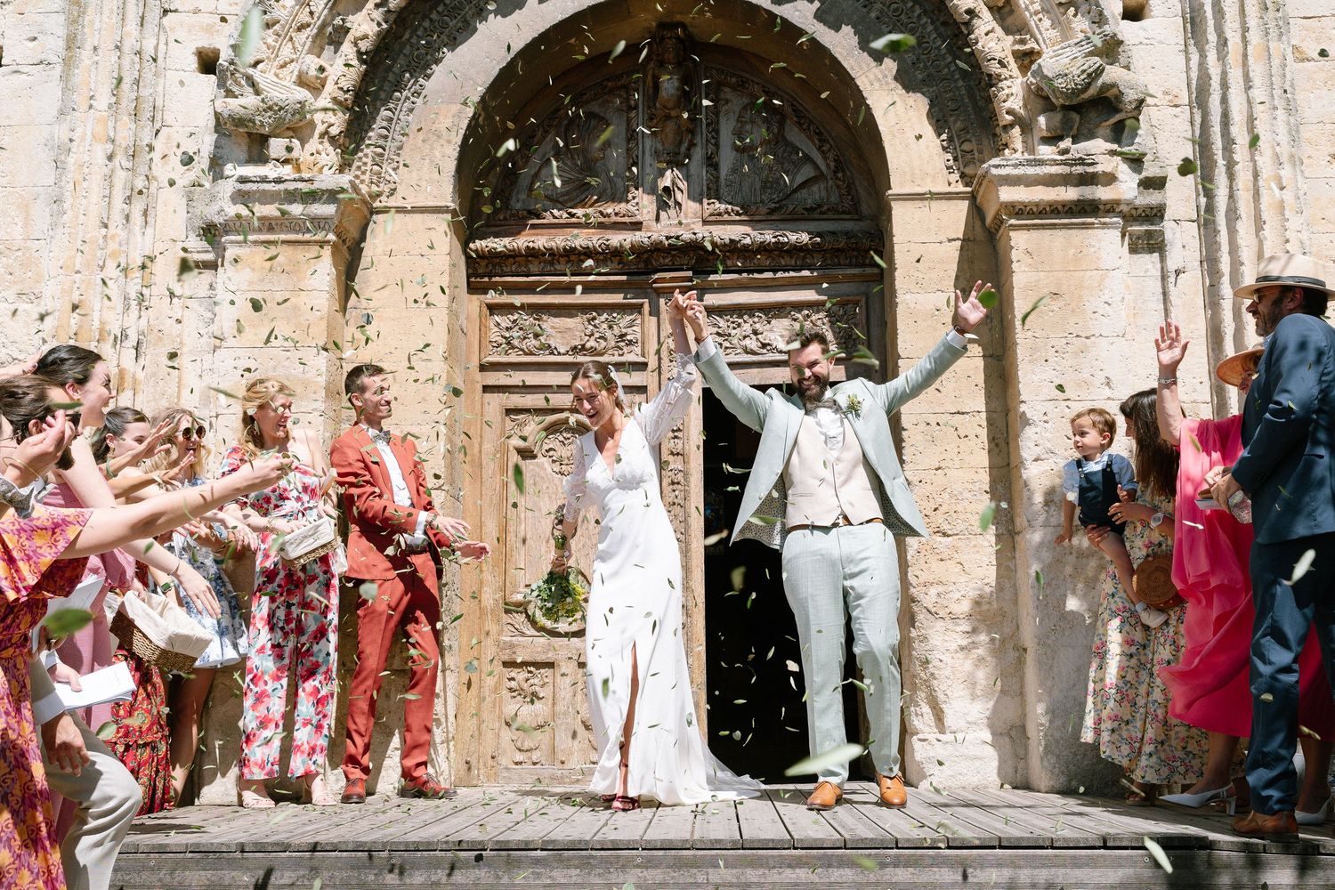 Wedding celebration outside historic stone archway with guests throwing confetti.
