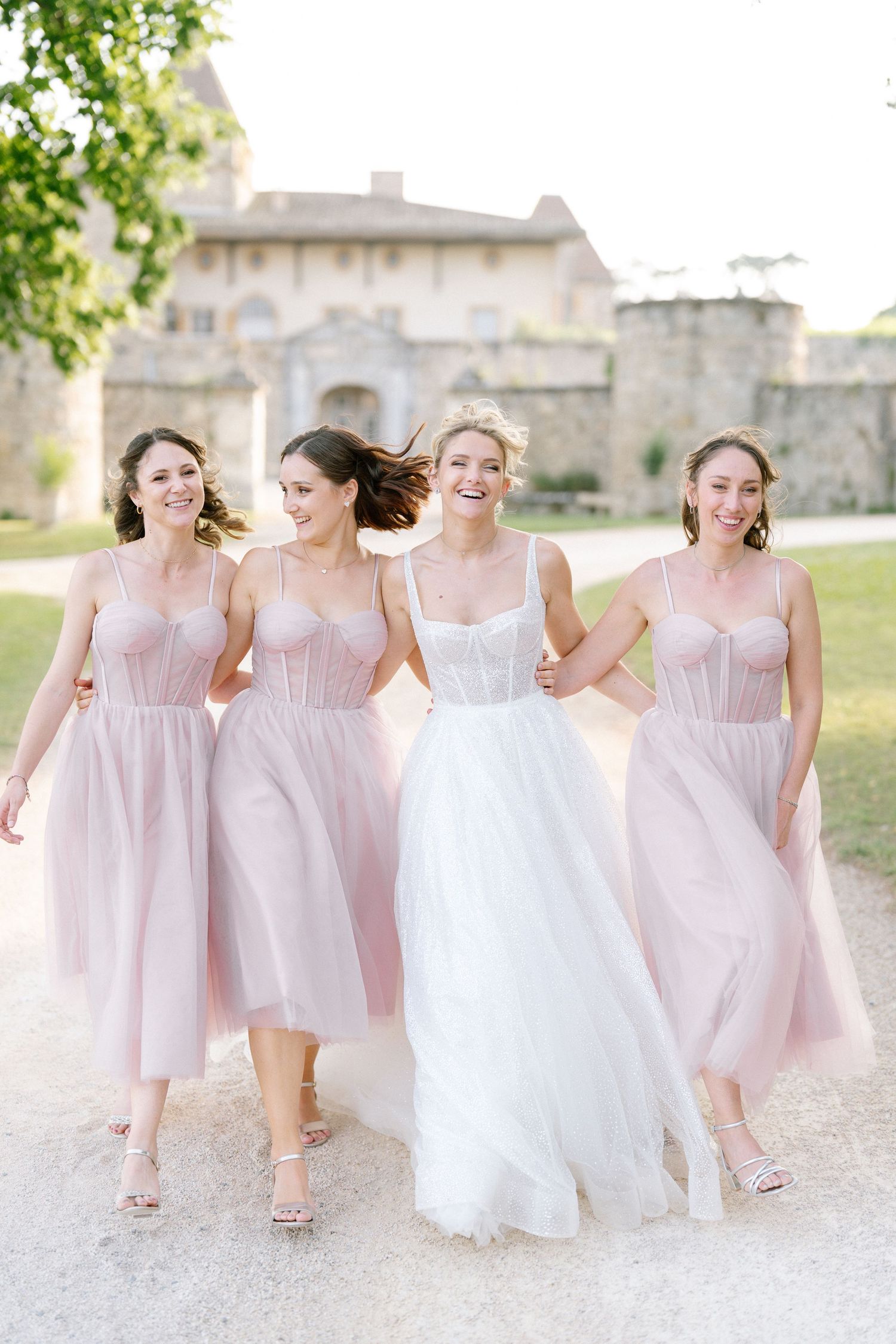 Bridesmaids in light pink dresses walk together on a path at a wedding venue.