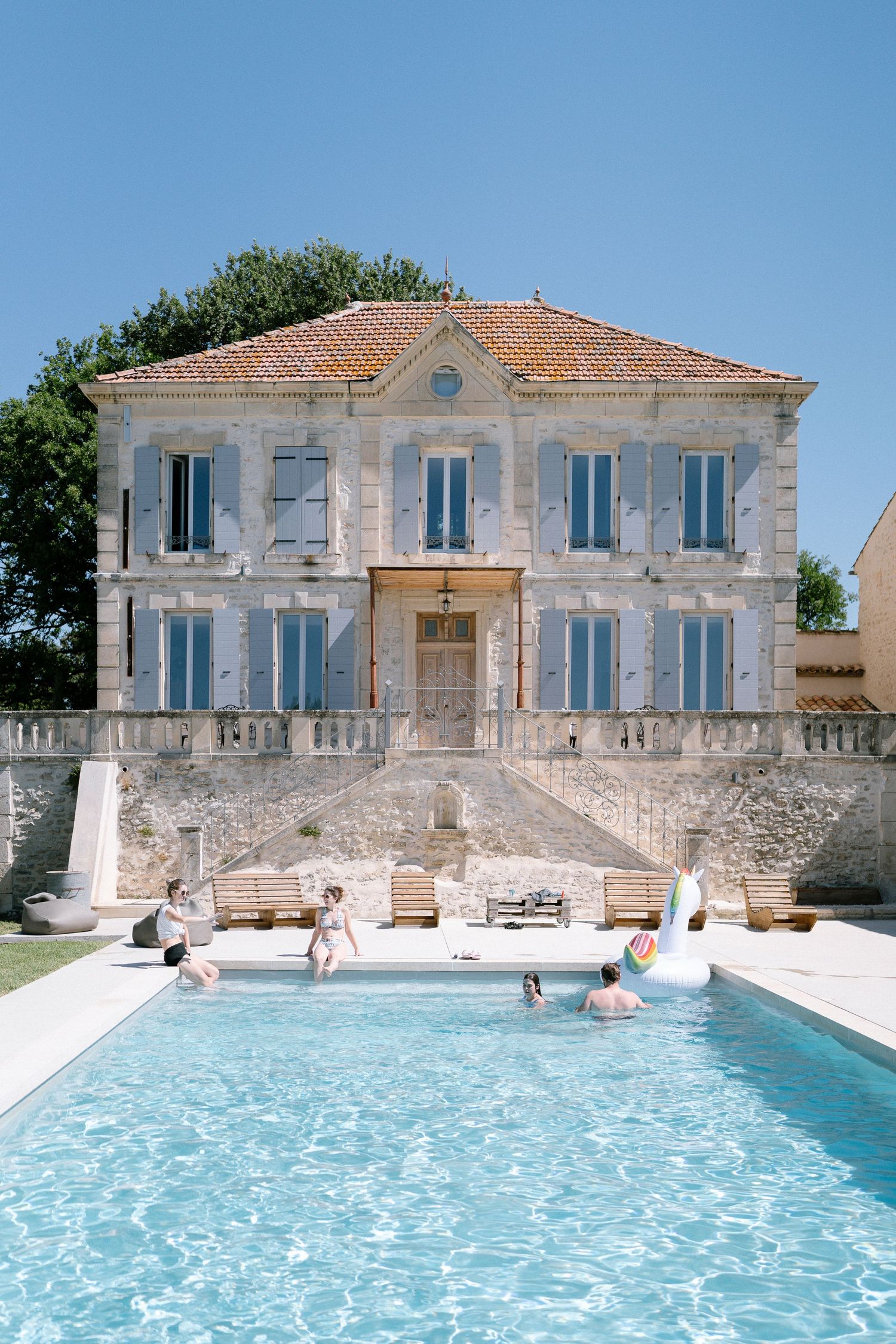 Elegant French country house with blue shutters and a pristine swimming pool in the foreground.