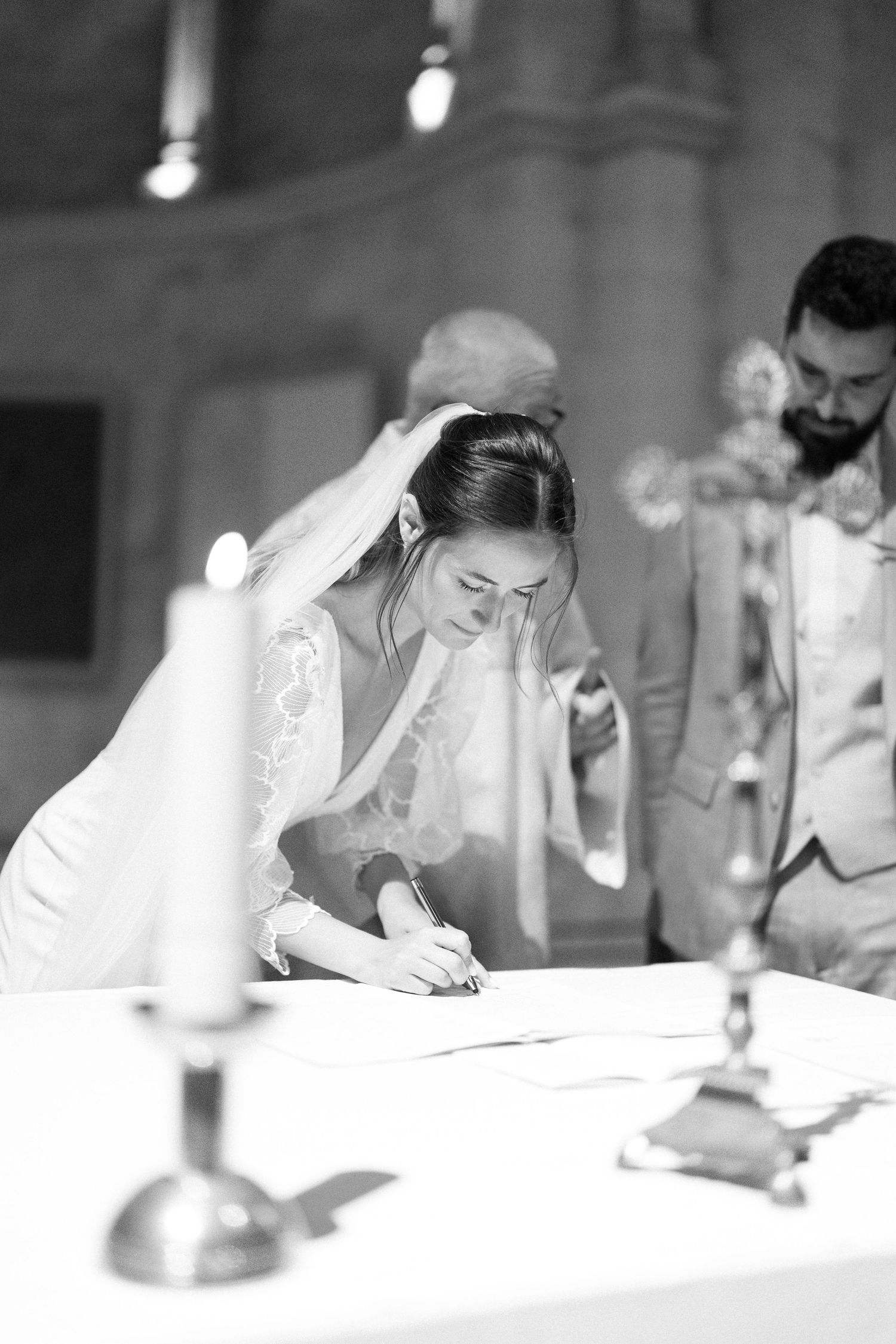 Wedding ceremony participants signing documents at a white table in a church setting.