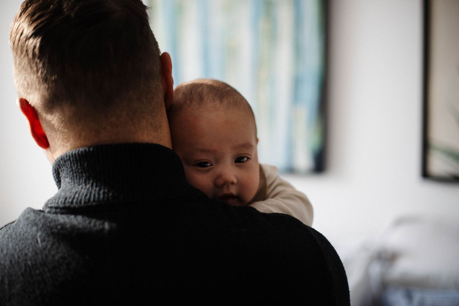 Candid moment of dad cuddling his baby in natural window light