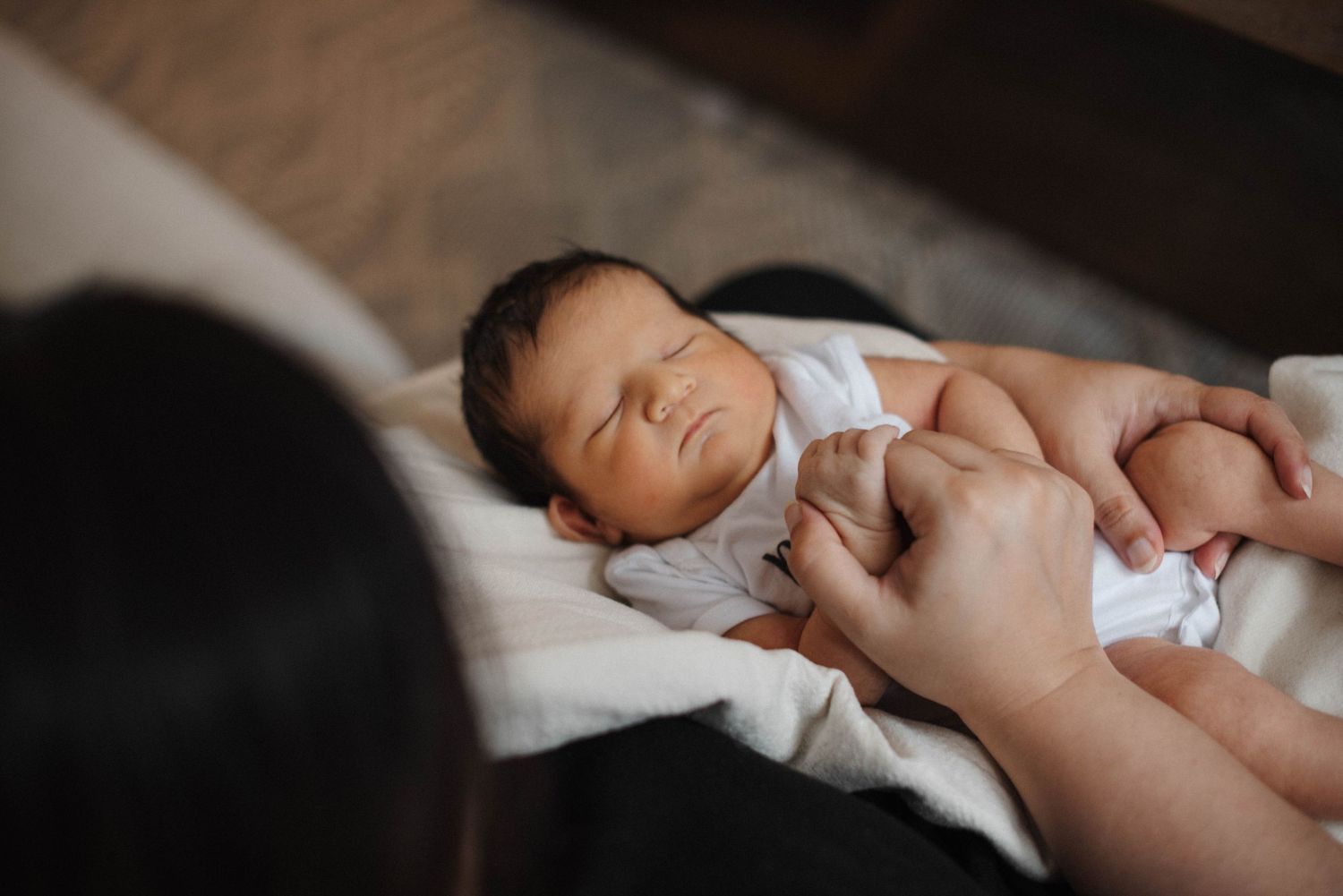 Mississauga in-home newborn photography capturing baby resting in mom's arm holding her finger