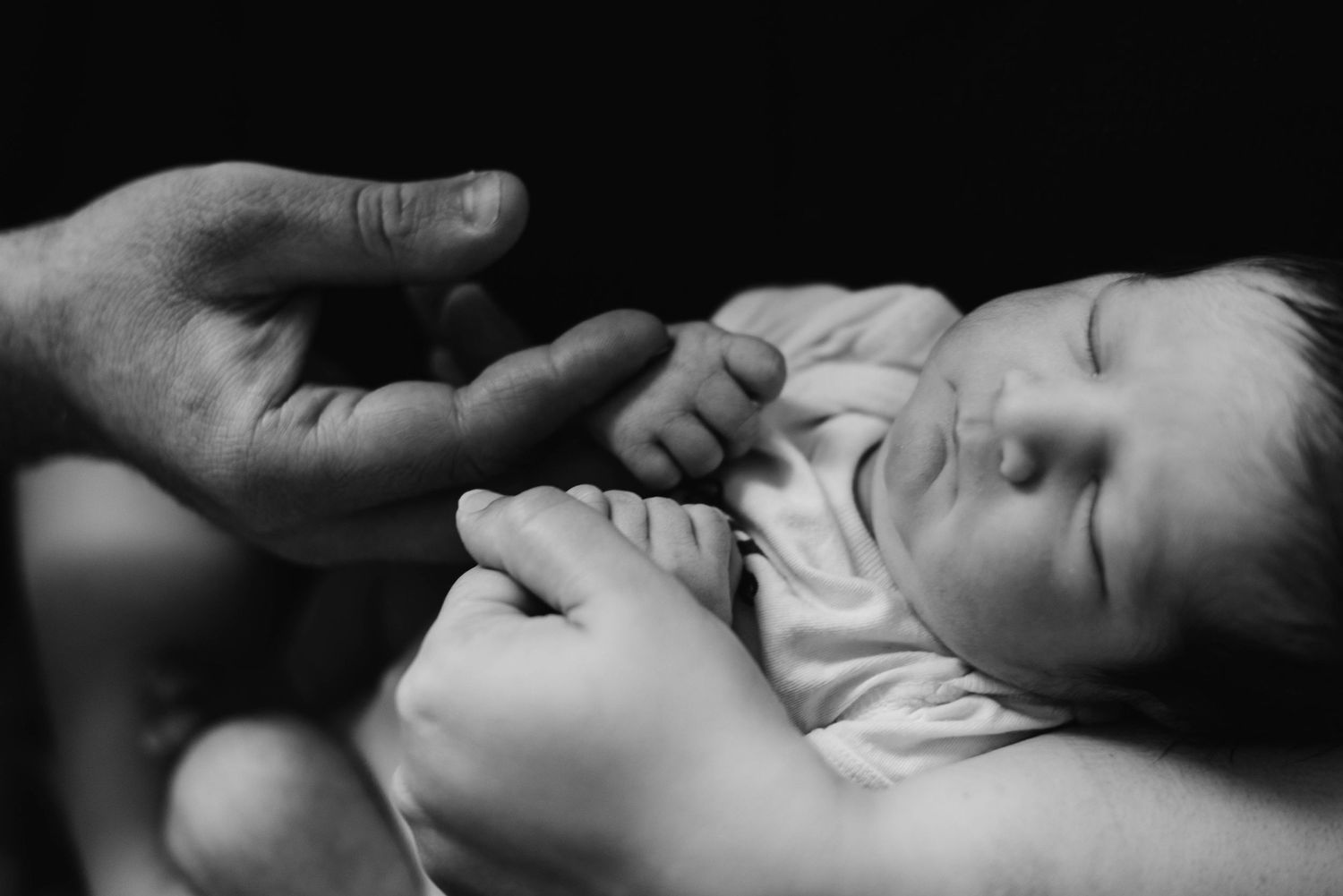 Newborn cradled in mother’s arms with older brother nearby during in-home lifestyle photography session in Oakville