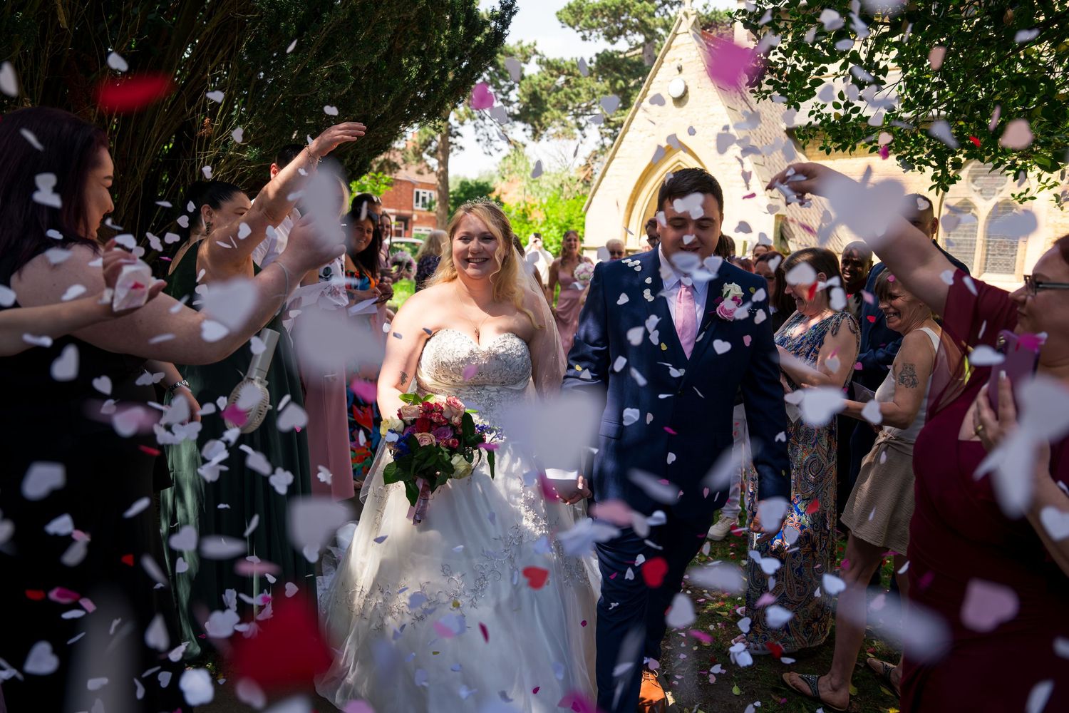 Bride and groom walk through confetti shower outside church after wedding ceremony.
