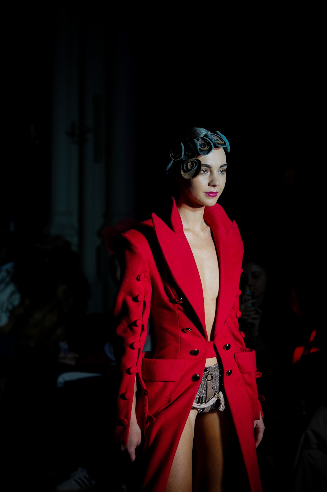 Model walks runway in dramatic red double-breasted coat with black buttons during fashion show presentation.