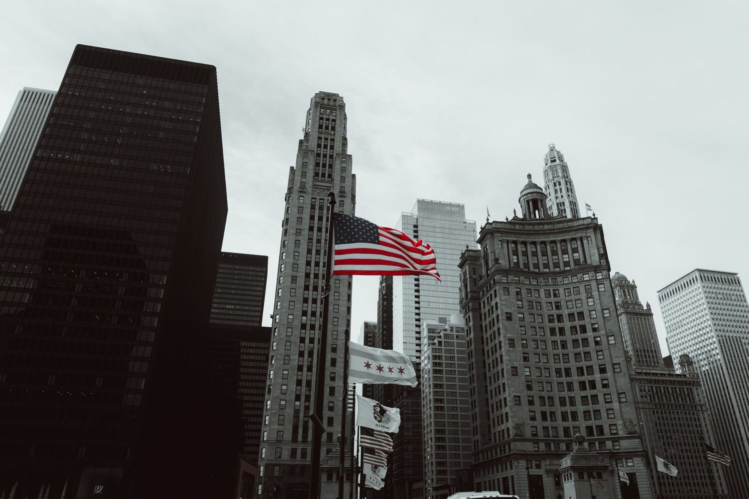 Stadsfoto van de skyline van Chicago met Amerikaanse vlag, historische en moderne wolkenkrabbers onder een bewolkte lucht.