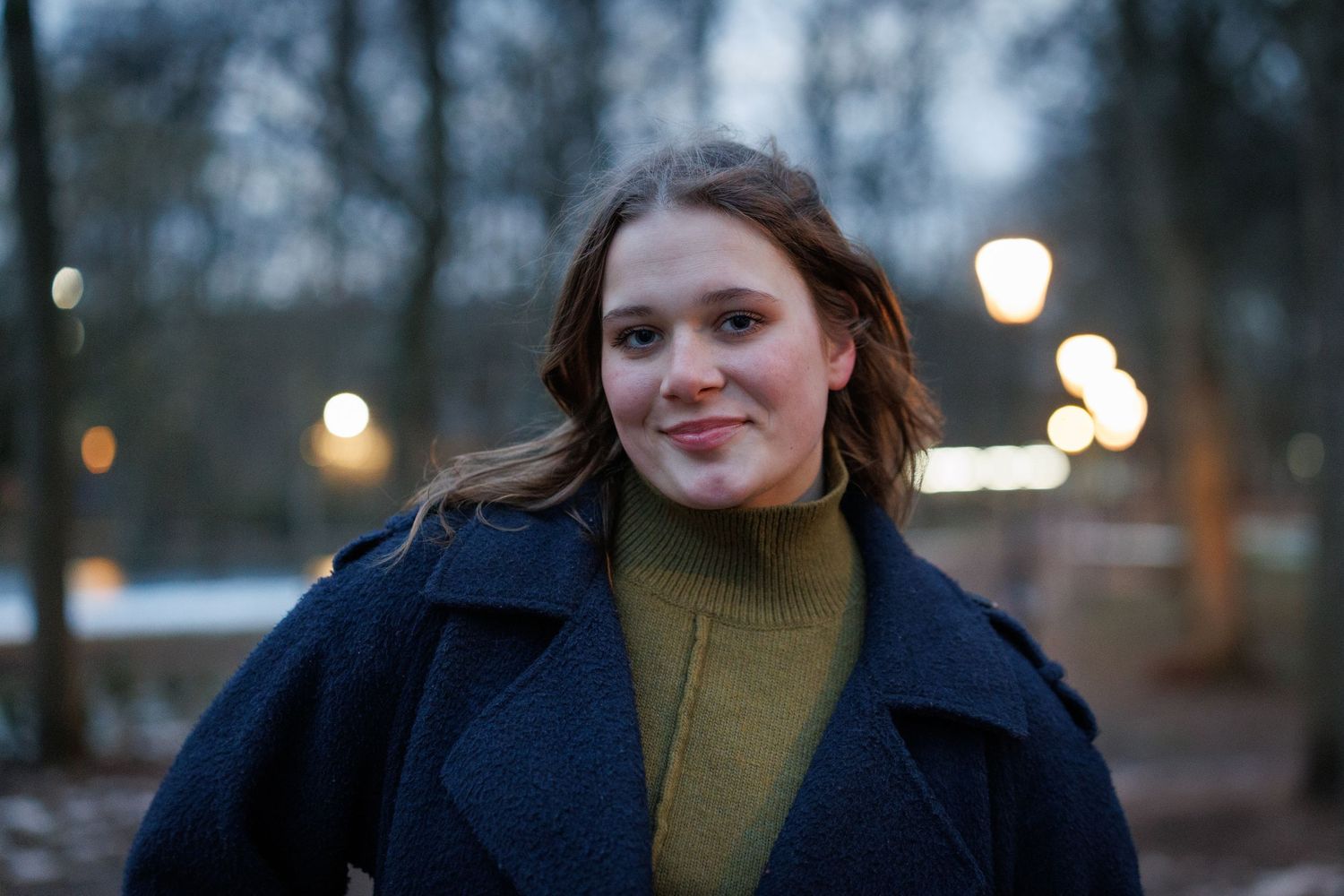 Portretfoto van een vrouw in een winterpark met sneeuw, vastgelegd met natuurlijk licht en zachte achtergrondonscherpte.