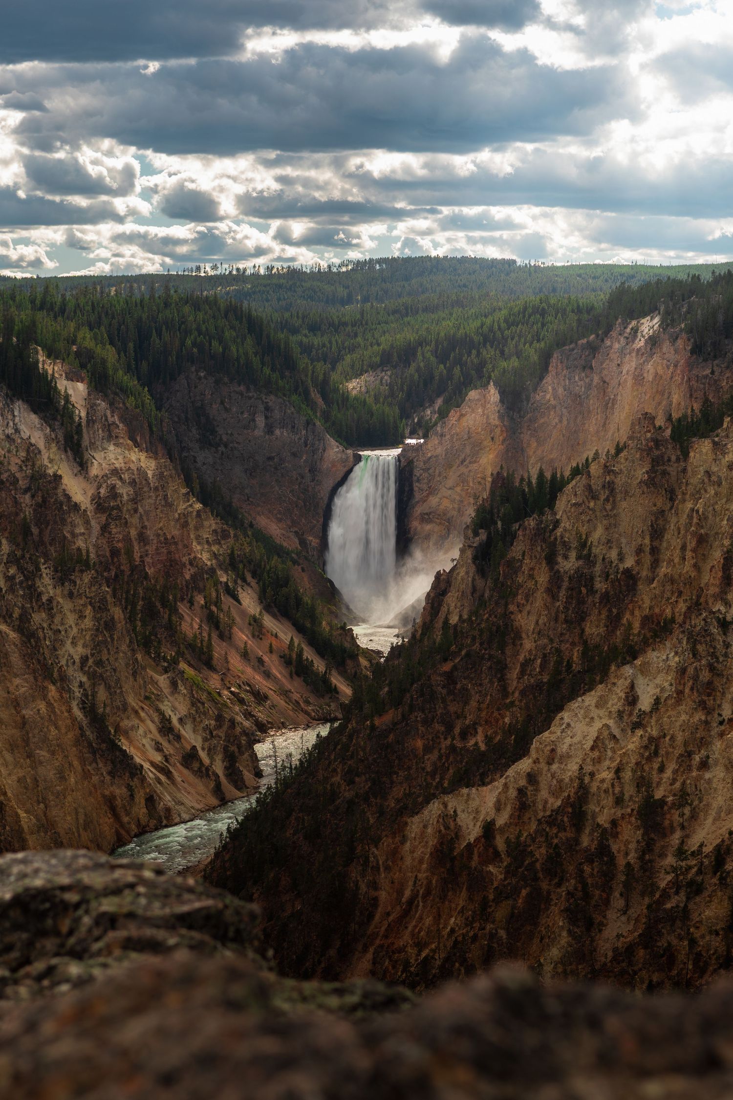 Landschapsfoto van Yellowstone National Park met waterval in een diepe kloof, rotswanden en dramatische lucht.