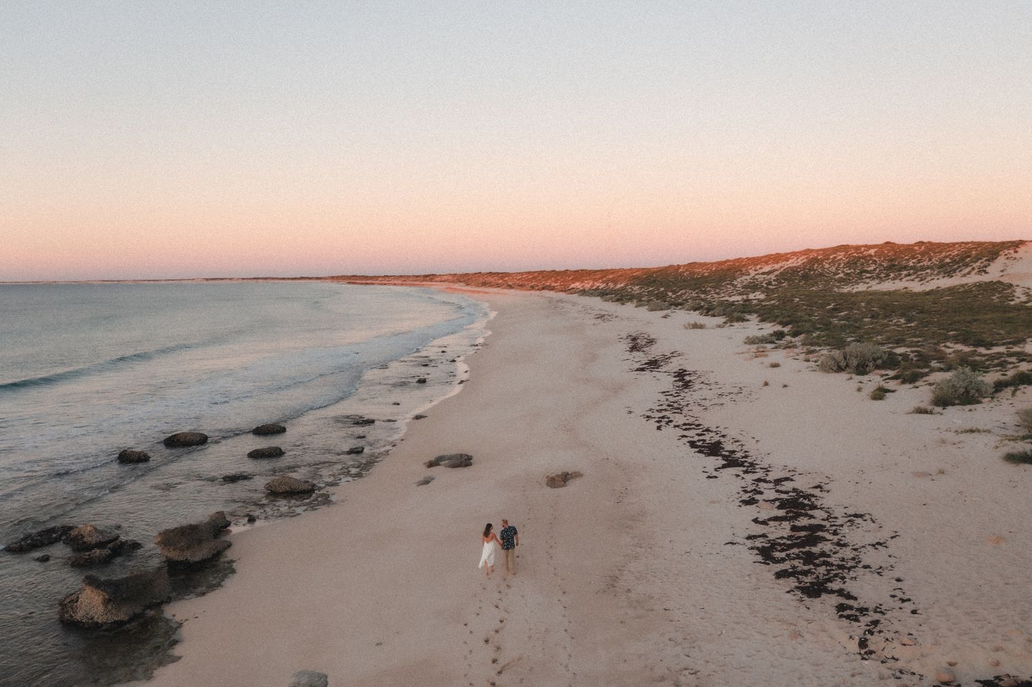 Drone photo of couple walking down the beach at sunset after elopement wedding ceremony