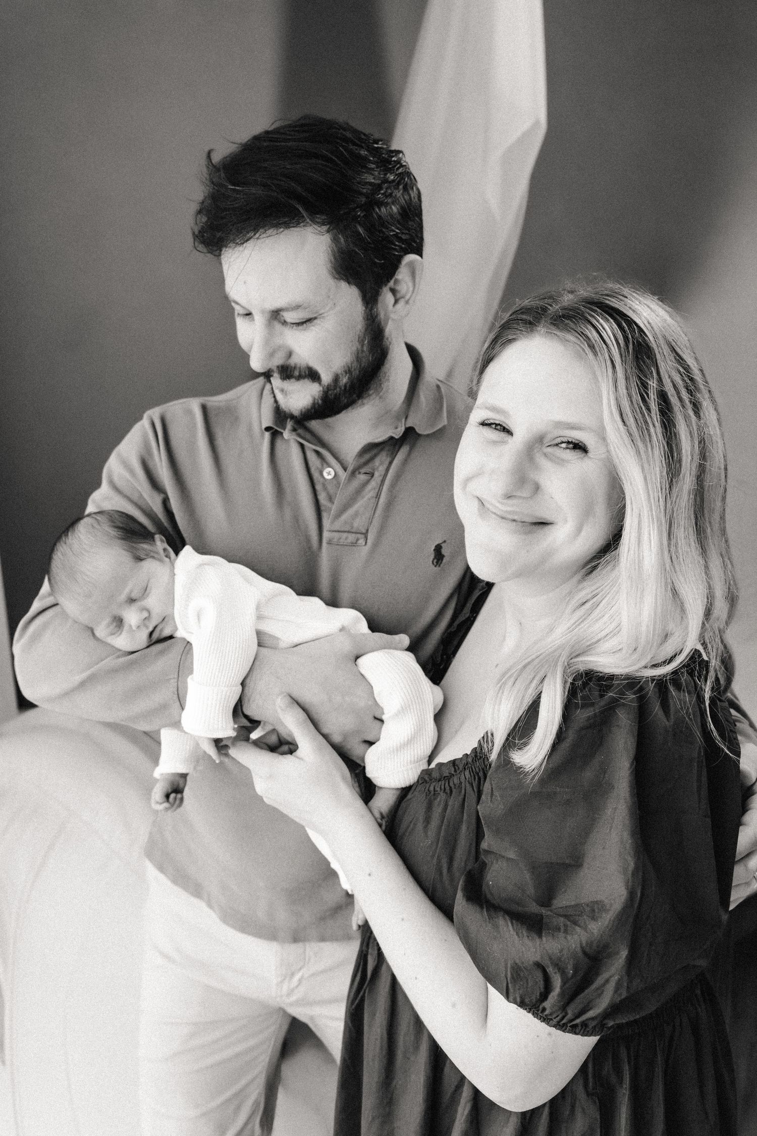 Couple holds newborn near window during newborn photography session